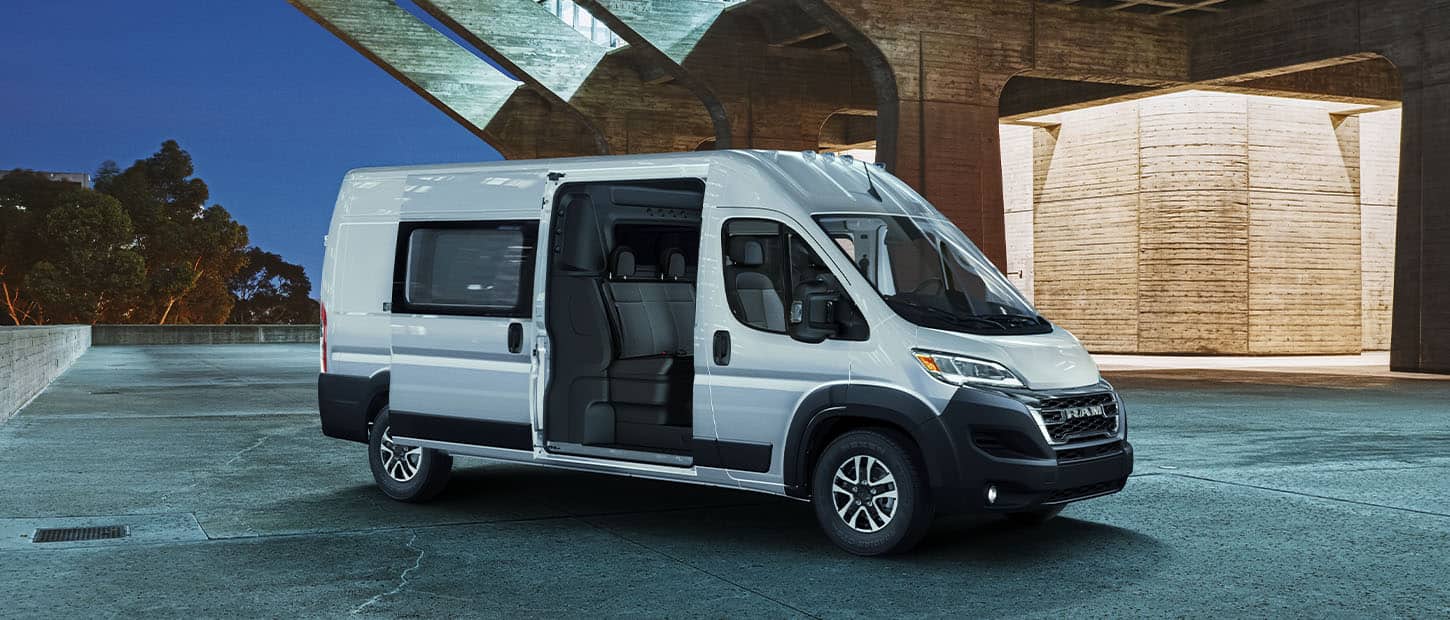 An angled passenger-side profile of a white 2024 Ram ProMaster SLT Crew Cargo Van High Roof with its passenger-side sliding door open, revealing a second row of seats.