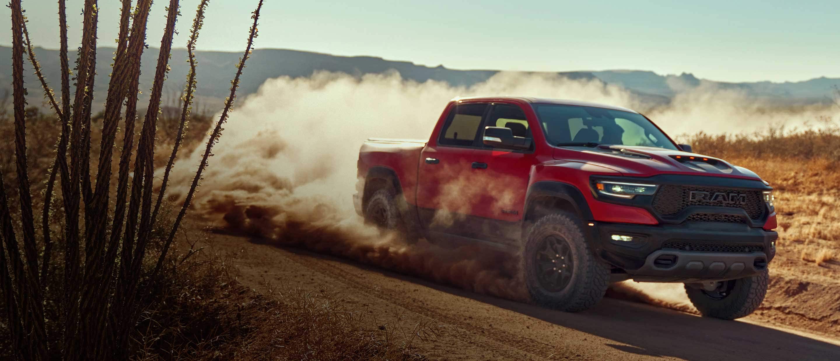 The 2024 Ram 1500 TRX being driven off-road in the desert on a dirt road with dust rising from its wheels.