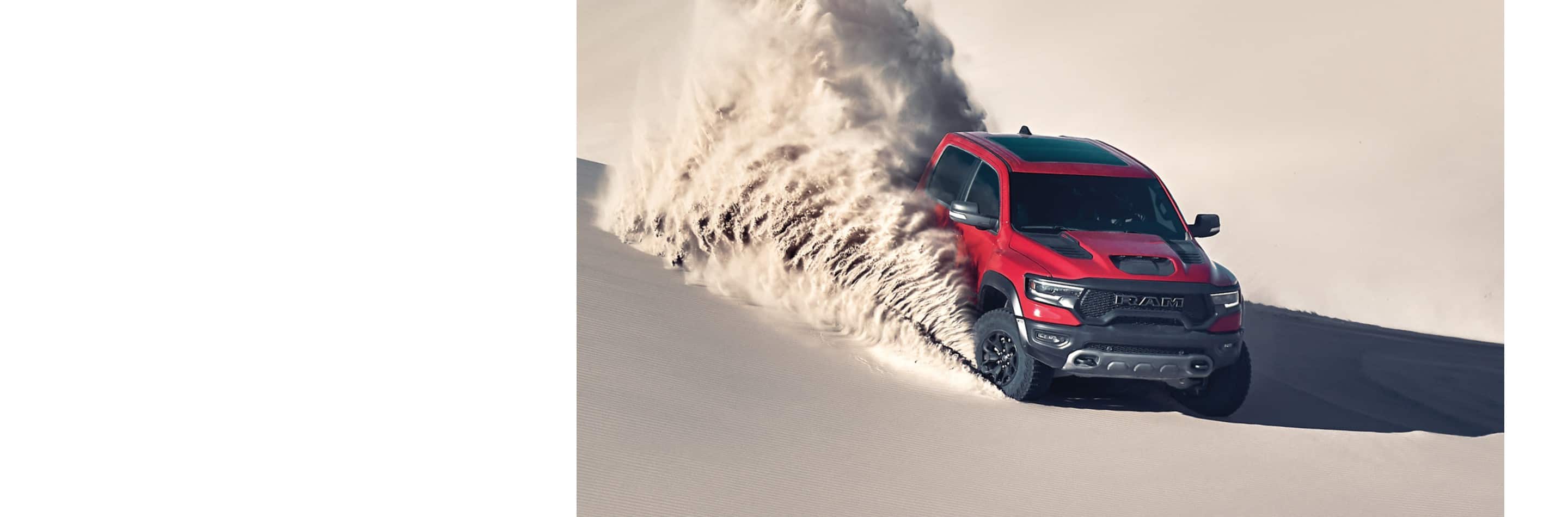 A red 2024 Ram 1500 TRX Crew Cab being driven off-road in the desert, descending a dune, with a cloud of dust and sand billowing from its wheels.