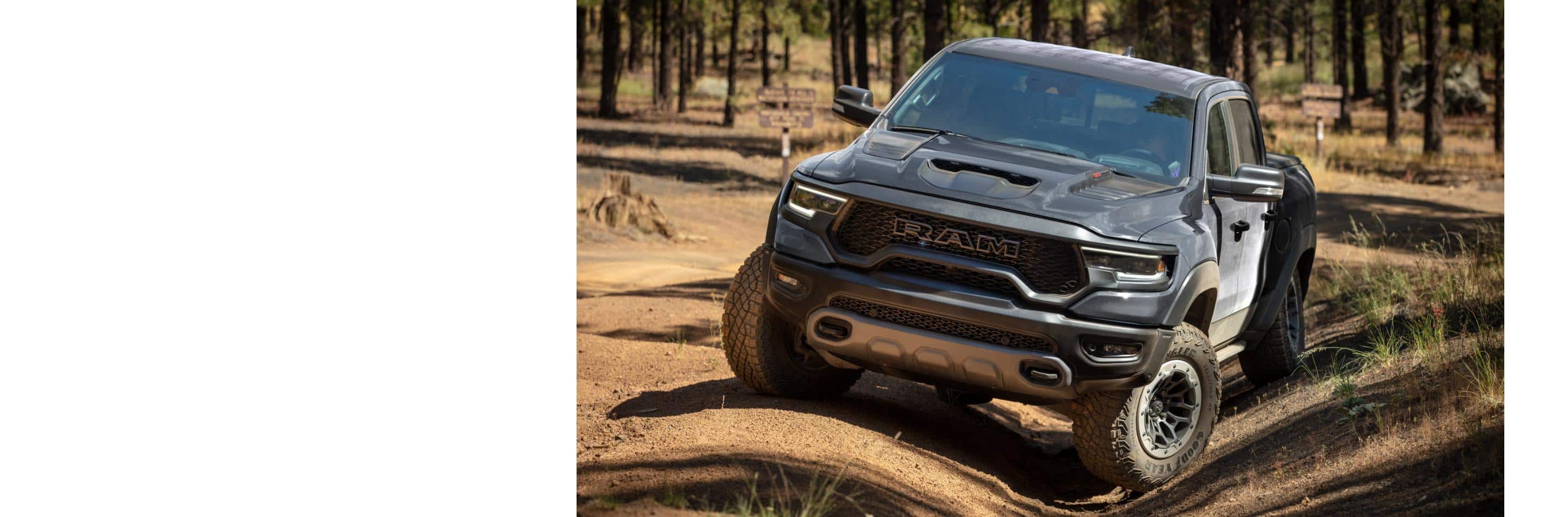 The 2024 Ram 1500 TRX Crew Cab being driven off-road on uneven terrain, with the front driver-side wheel in a shallow ditch and the other wheels elevated.
