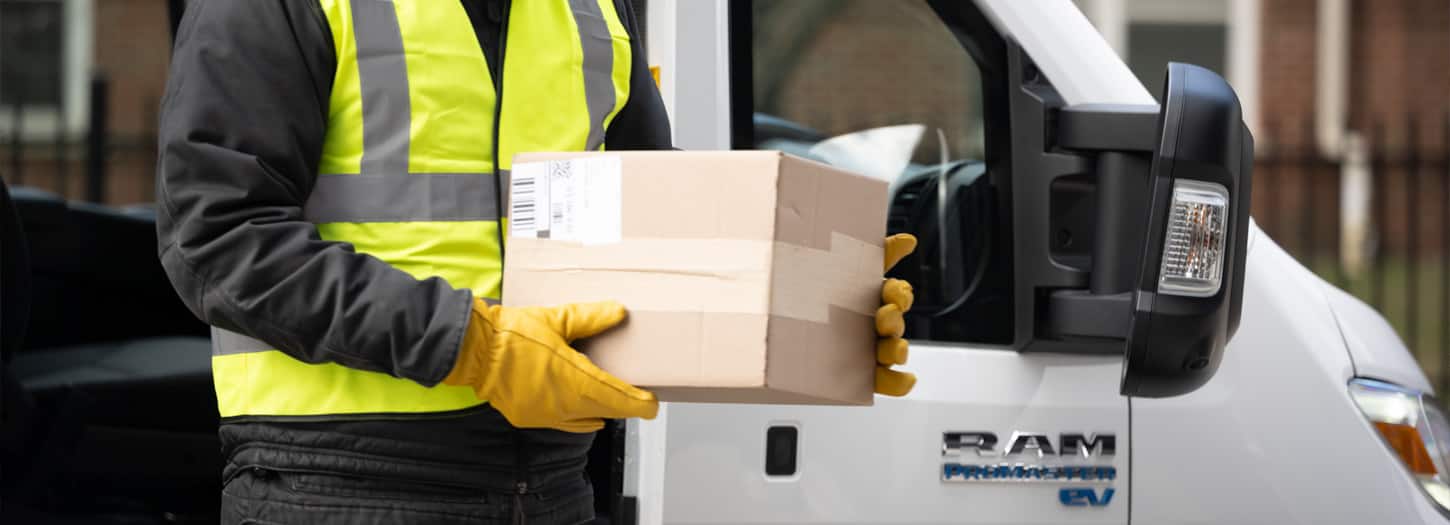 A person carrying a package as they walk alongside a white 2025 Ram ProMaster EV.