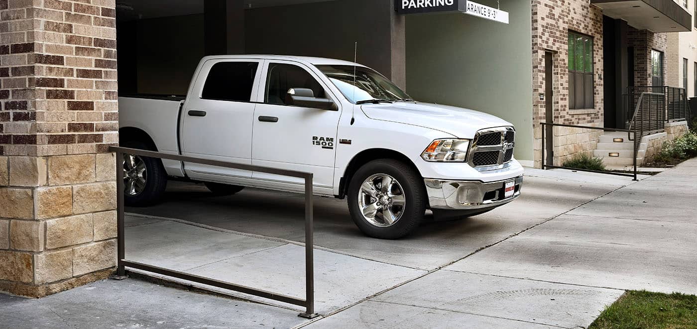 Display A white 2024 Ram 1500 Classic Tradesman Crew Cab pulling out of a commercial garage.