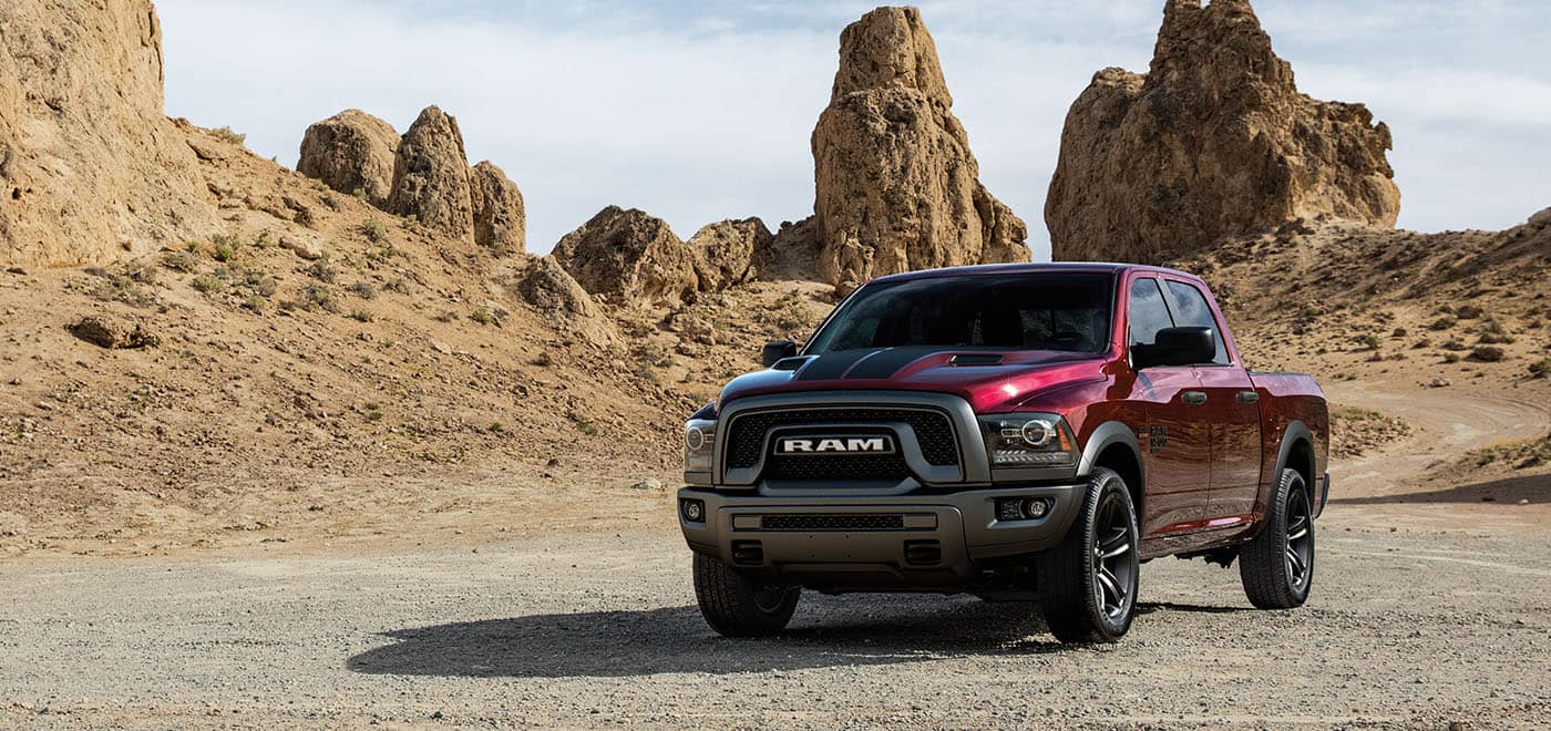 Display A red 2024 Ram 1500 Classic Warlock 4x4 Crew Cab parked on a twisting desert road with rocky outcroppings in the distance.