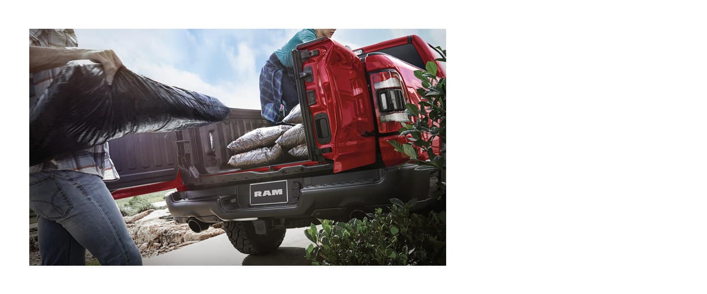 The pickup bed in a red 2024 Ram 1500 with its swing-away doors open as it's being loaded with landscaping materials.