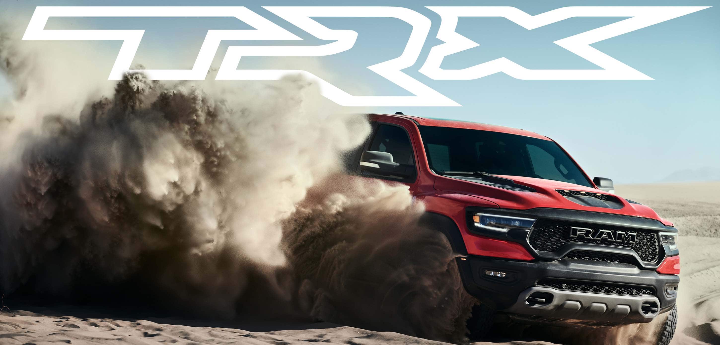The front angle of a red 2024 Ram 1500 TRX Crew Cab surrounded by a huge billowing cloud of dust emanating from its wheels as it is driven off-road on a sand dune. TRX.