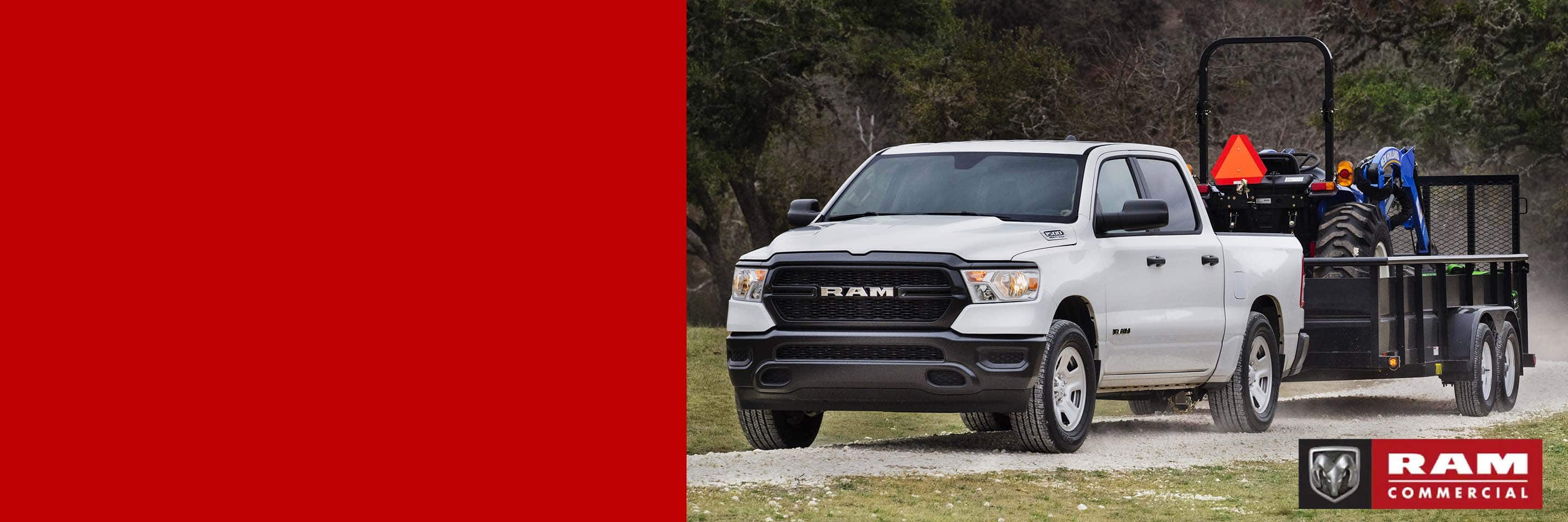 A white 2024 Ram 1500 Tradesman Crew Cab towing a tractor in a landscape trailer. Ram Commercial.