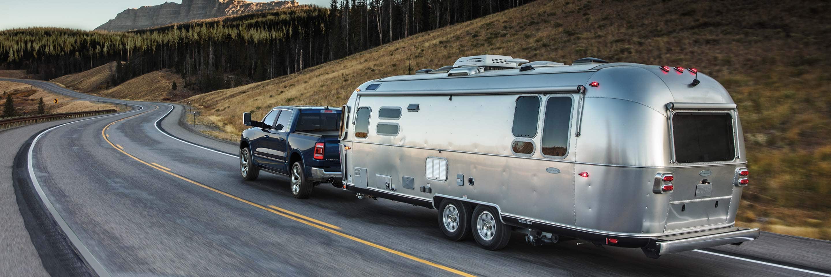 A black 2024 Ram 1500 Limited Crew Cab towing a large travel trailer as it is driven on a winding highway through the mountains.
