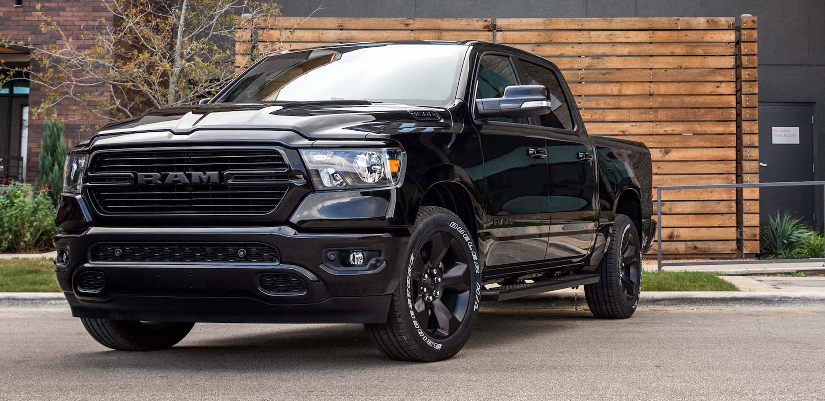 Display A front angled driver-side profile of a black 2024 Ram 1500 Laramie Crew Cab parked in front of a horizontal wooden fence.