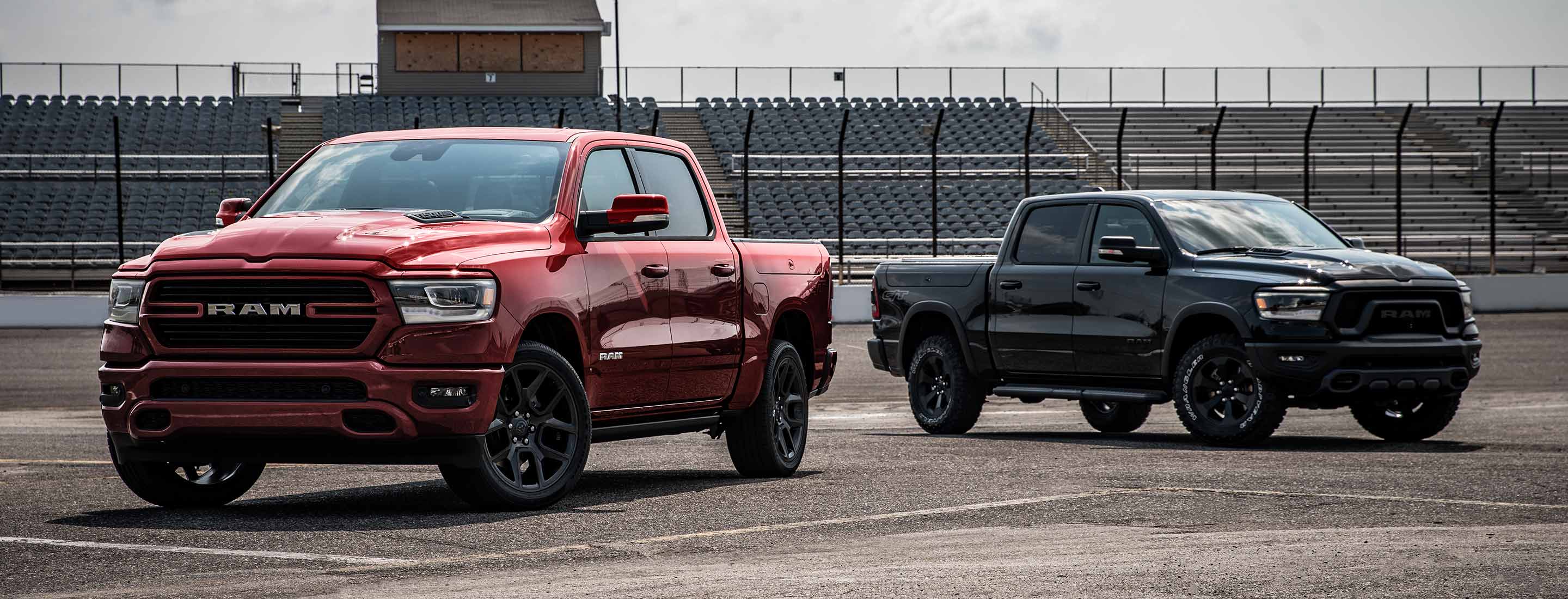 Two Ram 1500 models parked at a racetrack. On the left, a red 2024 Ram 1500 Laramie G/T Crew Cab and on the right, a black 2024 Ram 1500 Rebel G/T Crew Cab.