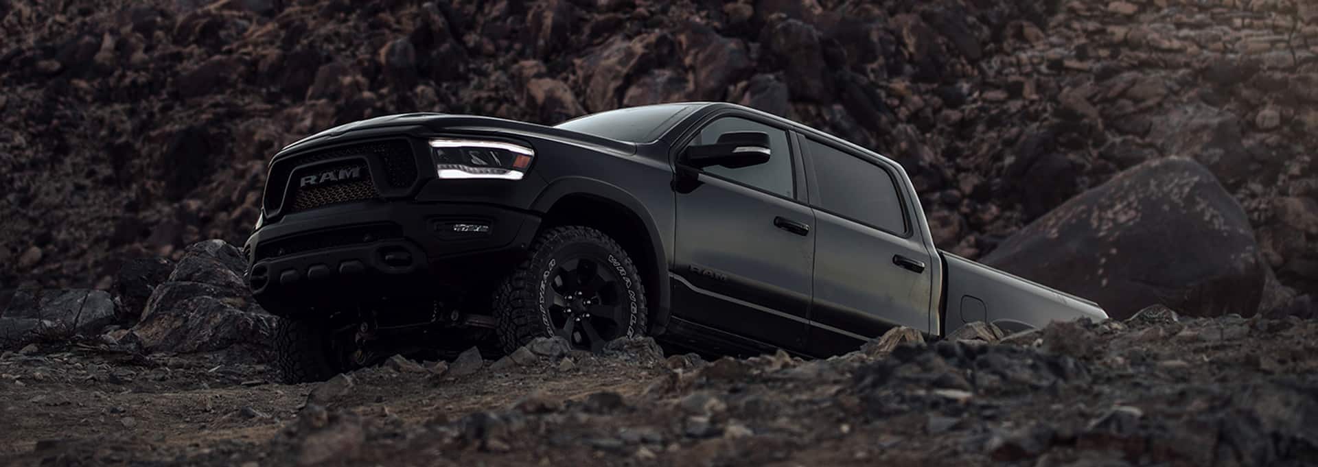 An angled driver-side profile of a black 2024 Ram 1500 Rebel Night Edition climbing up a rocky hill off-road.