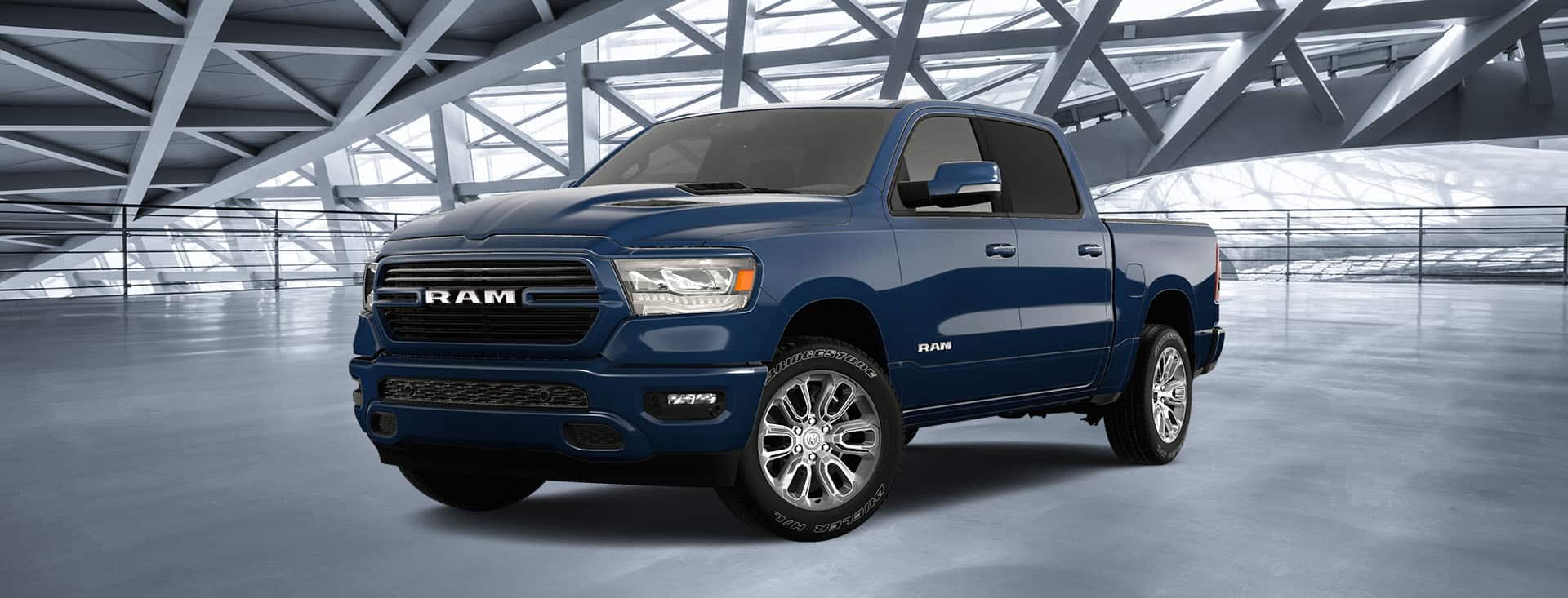 An angled driver-side profile of a blue 2024 Ram 1500 Laramie with the Sport Appearance Package, parked in a contemporary parking structure.