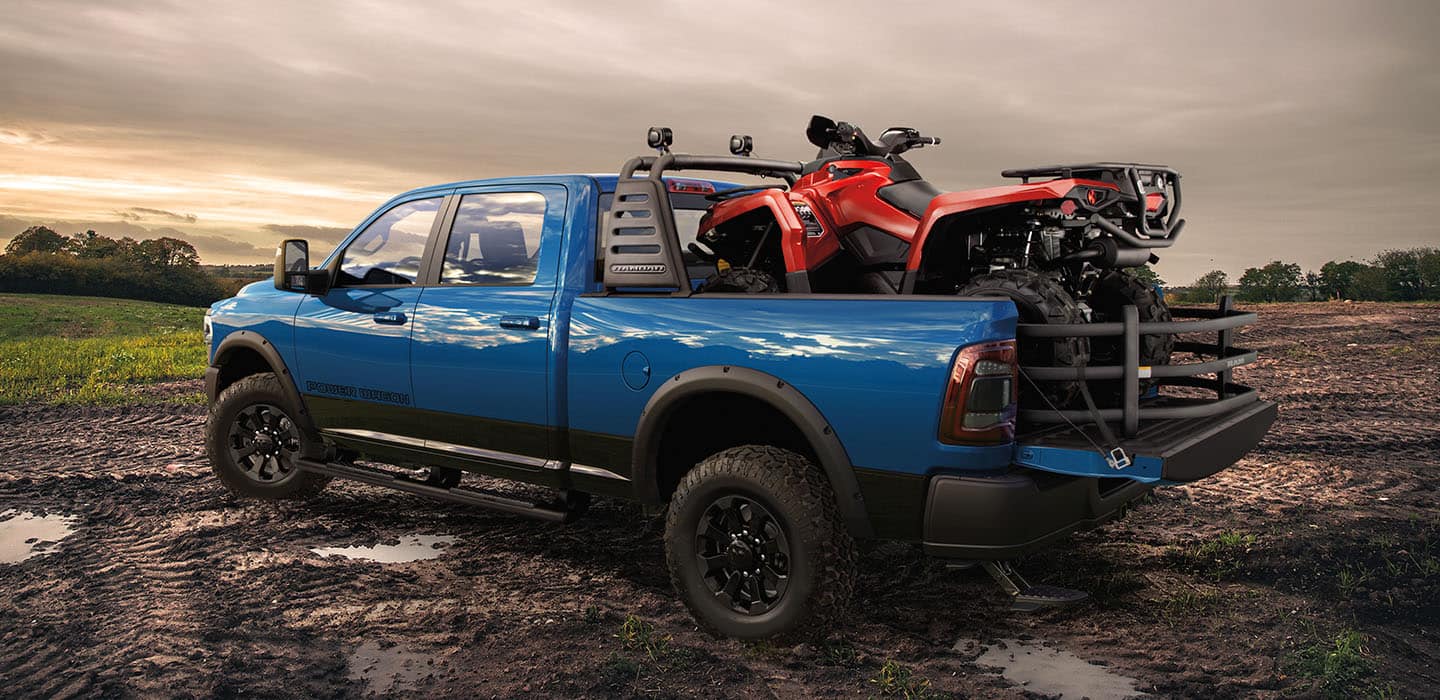a blue truck parked in a muddy field with an ATV in the bed