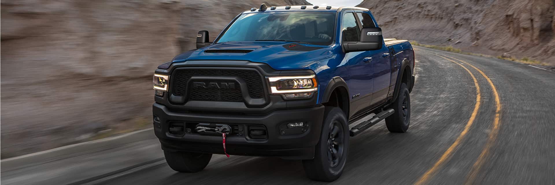 A blue 2024 Ram 2500 Power Wagon being driven on a curve on the highway. The background is blurred to indicate the vehicle is in motion.