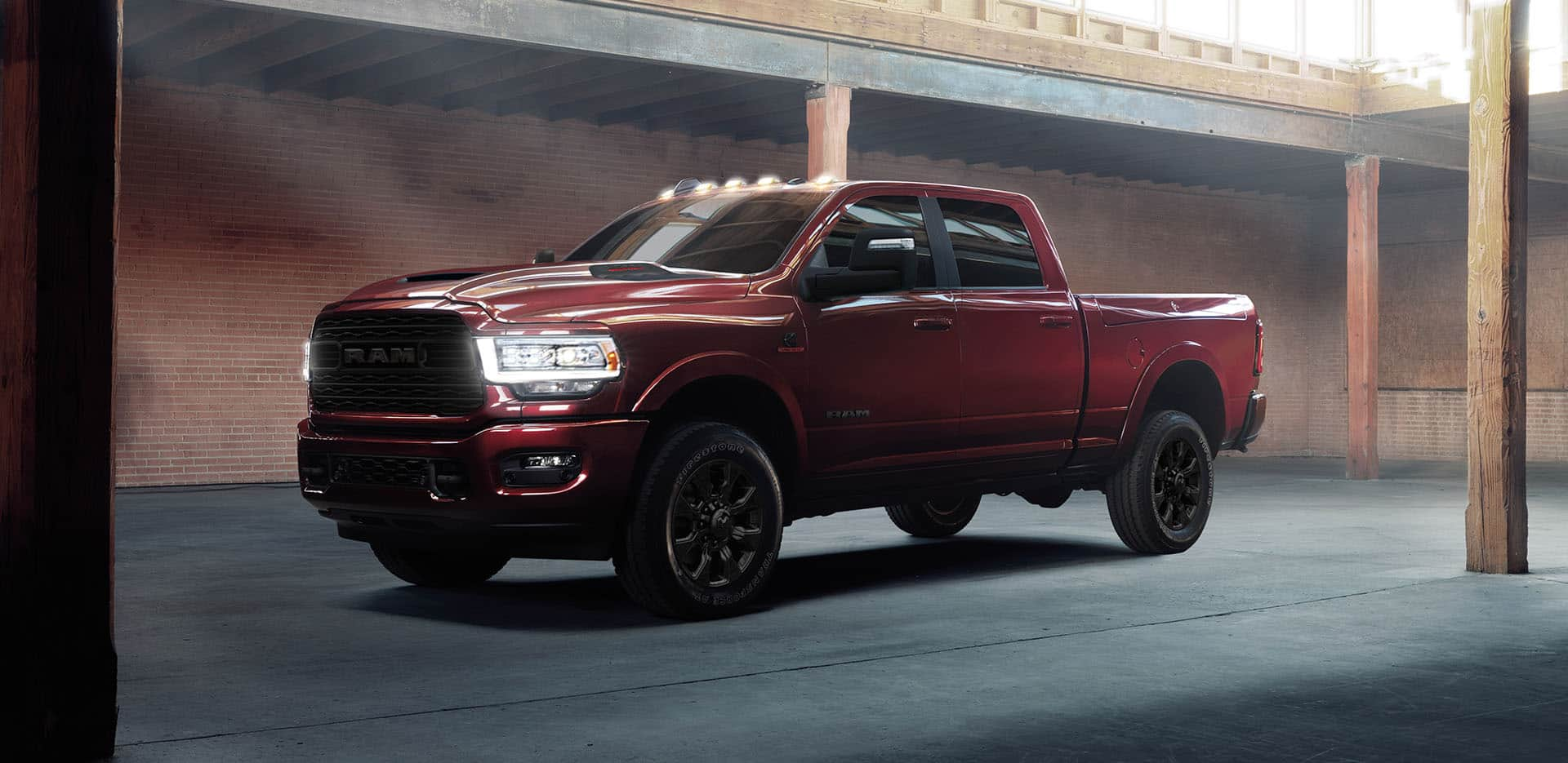 Display An angled driver-side profile of a red 2024 Ram 2500 Limited Crew Cab with its headlamps on, parked in a commercial garage.