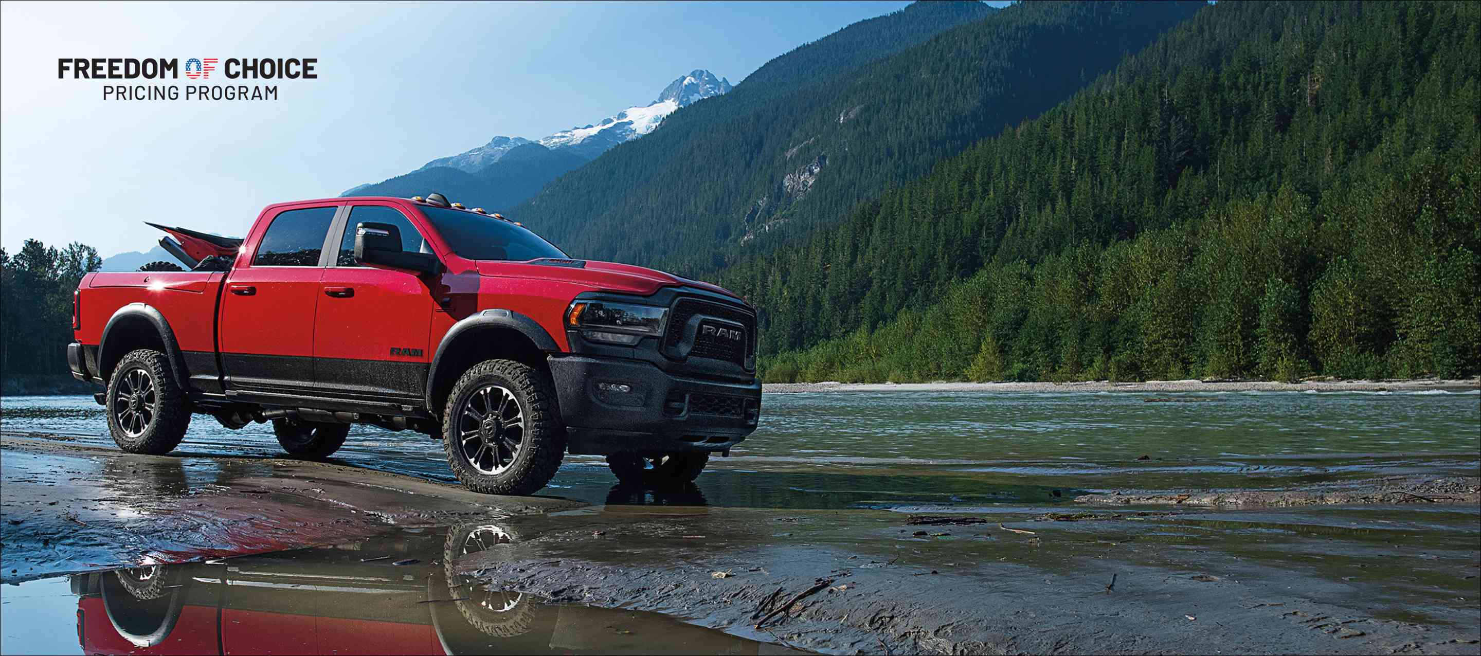 A red 2024 Ram 2500 Rebel 4x4 Crew Cab with an ATV in its pickup box, and mountains in the background.. Freedom Of Choice Pricing Update Sales Event.