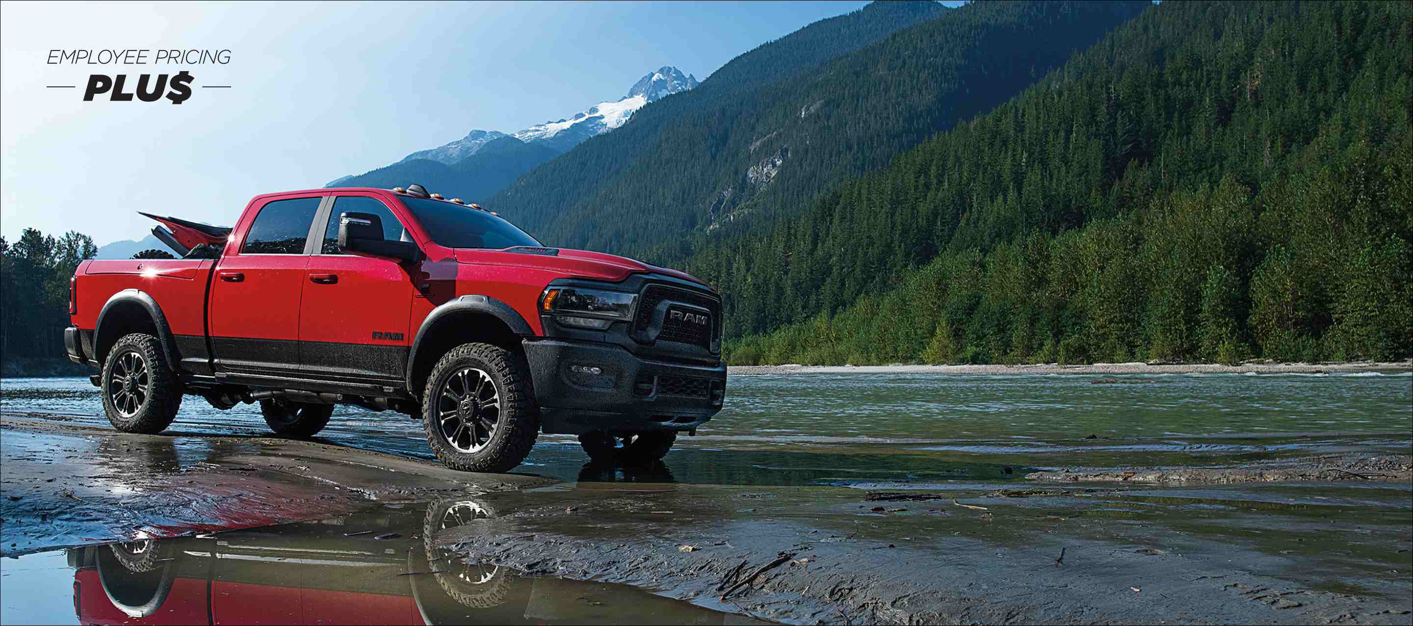 A red 2024 Ram 2500 Rebel 4x4 Crew Cab with an ATV in its pickup box, and mountains in the background. Employee Pricing Plus Sales Event.