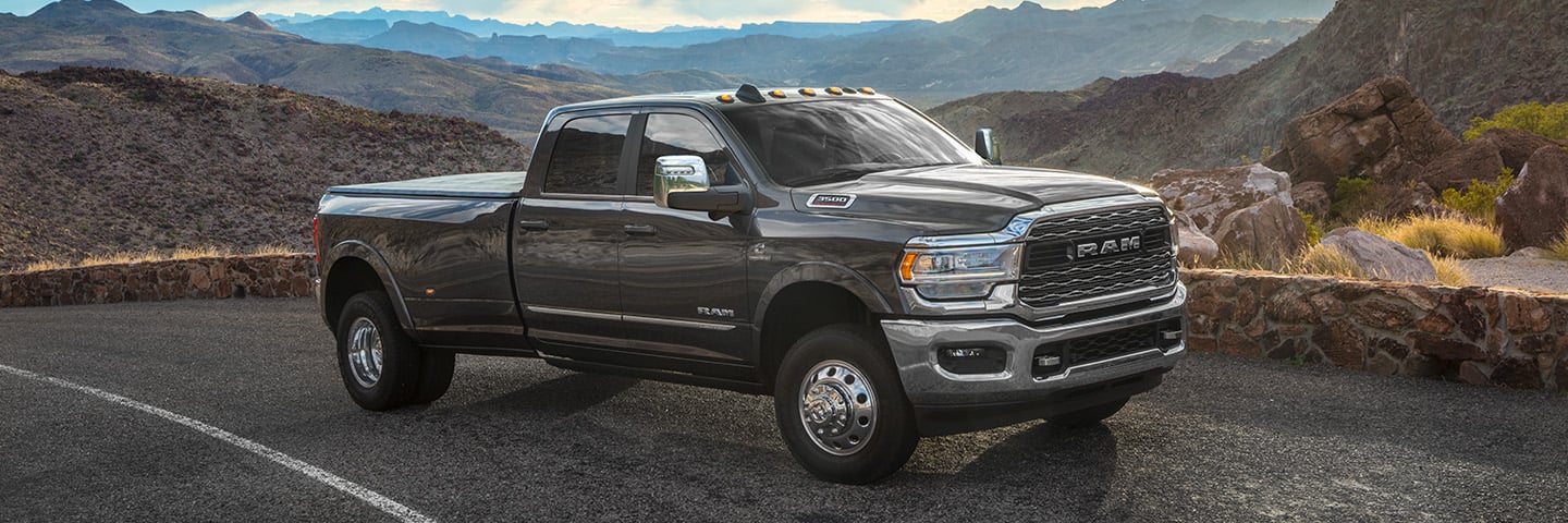 A gray 2024 Ram 3500 Limited Crew Cab parked on the side of the highway, overlooking a vast array of mountains.