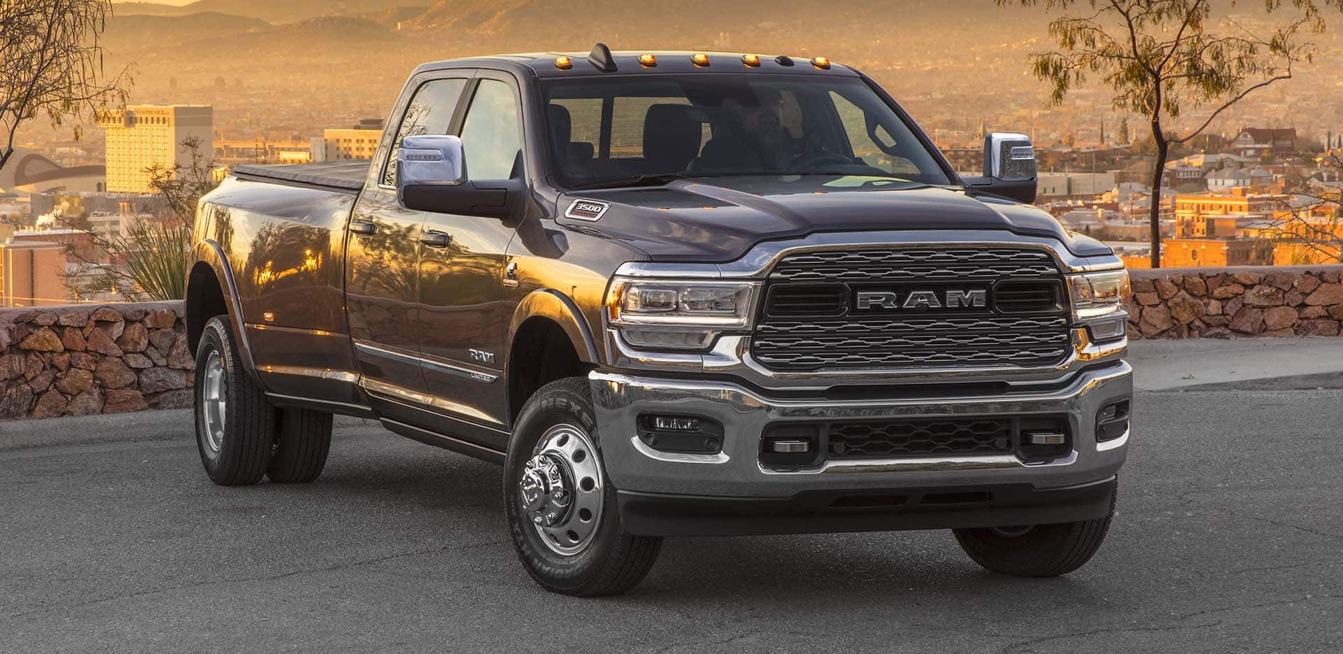 Display A gray 2024 Ram 3500 Limited Crew Cab parked in a lot on a hill, overlooking a cityscape.