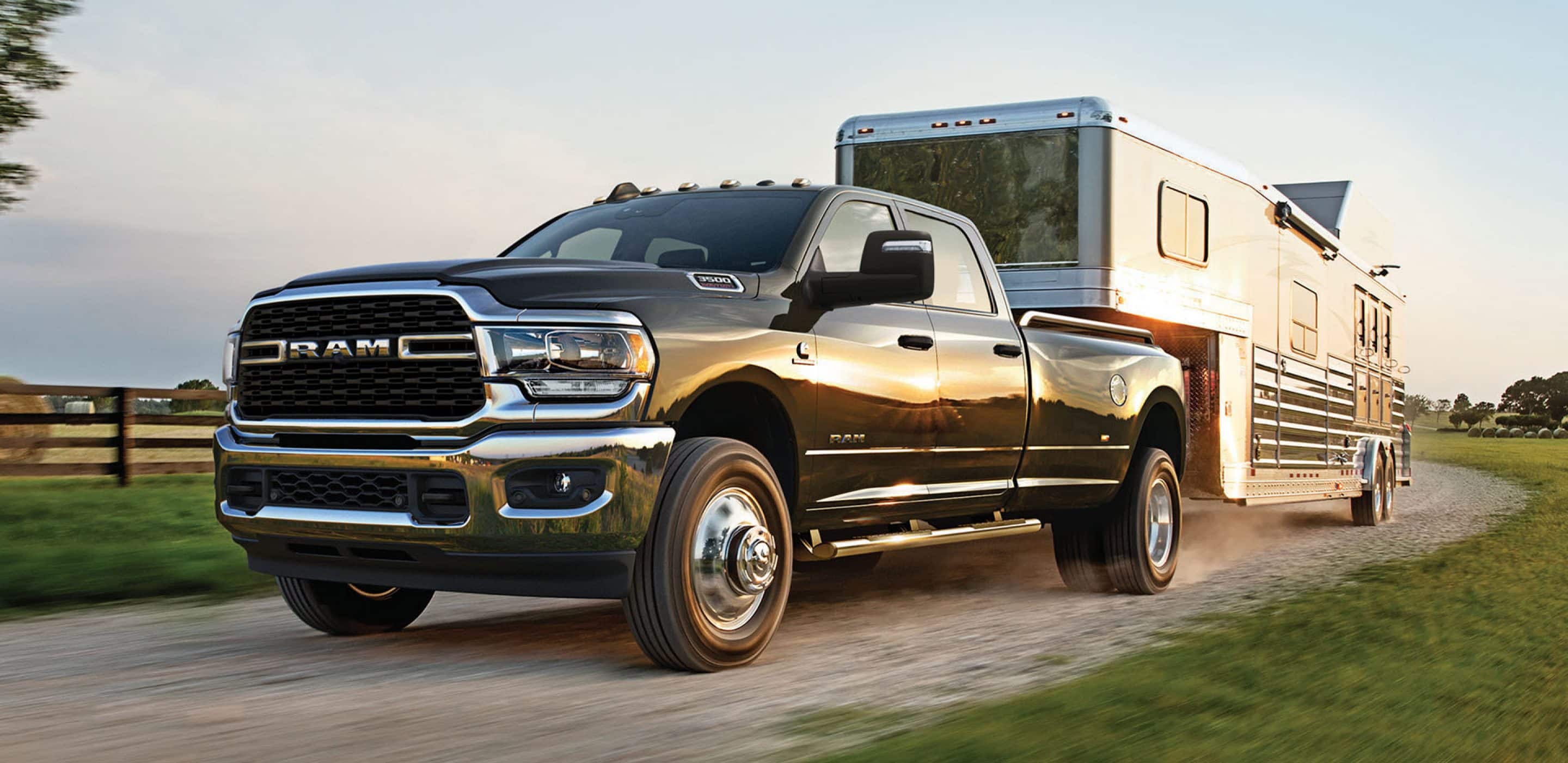 2024 RAM 3500 Big Horn in Diamond Black Crystal towing a black trailer on gravel road.