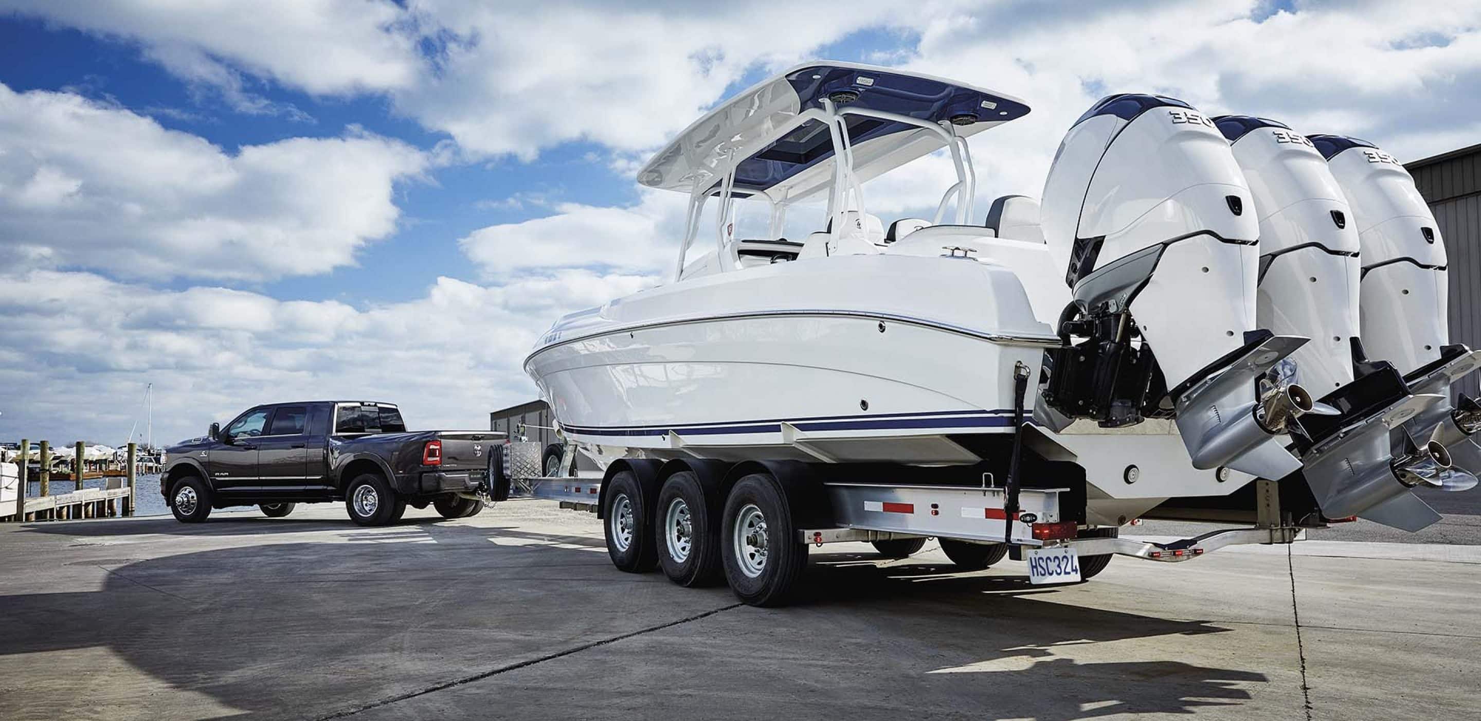 2024 RAM 3500 Tradesman in Granite Crystal towing a white boat with three motors.