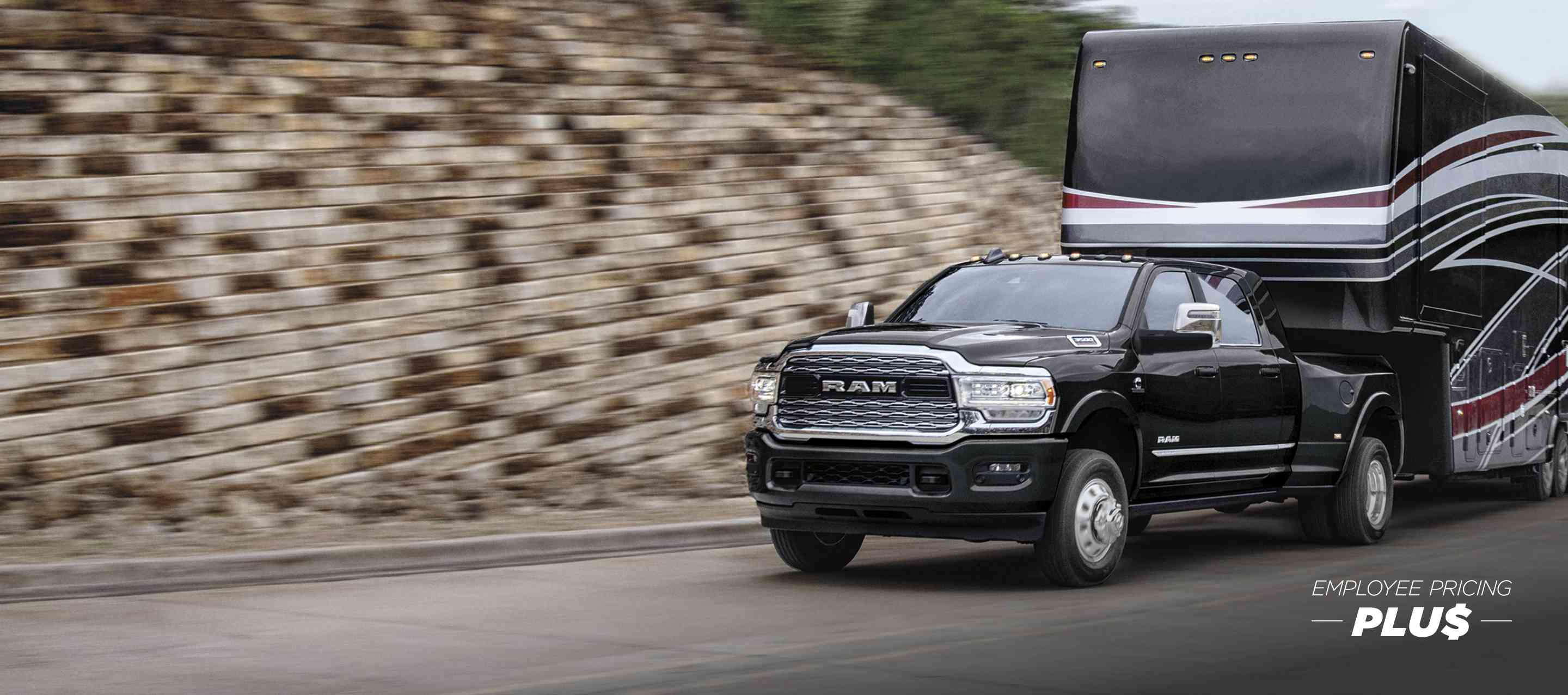 A black 2024 Ram 3500 Limited Mega Cab traveling down a highway, towing a large fifth wheel travel trailer. The background is blurred. Employee Pricing Plus Sales Event.