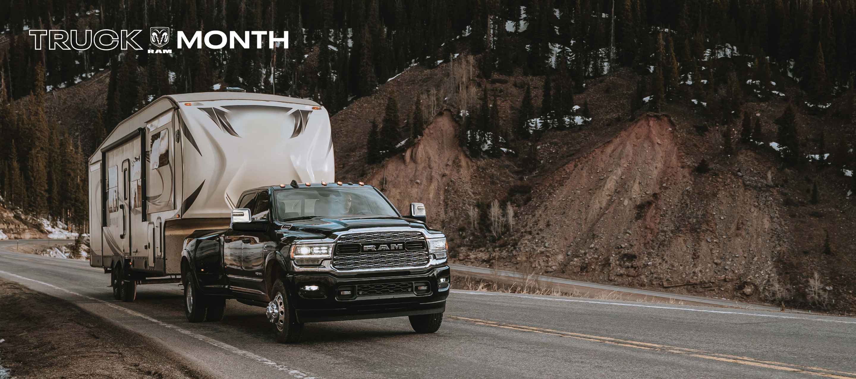 A black 2024 Ram 3500 Limited 4x4 Crew Cab towing a fifth wheel travel trailer as it is driven down a highway in the woods. Truck Month Sales Event.
