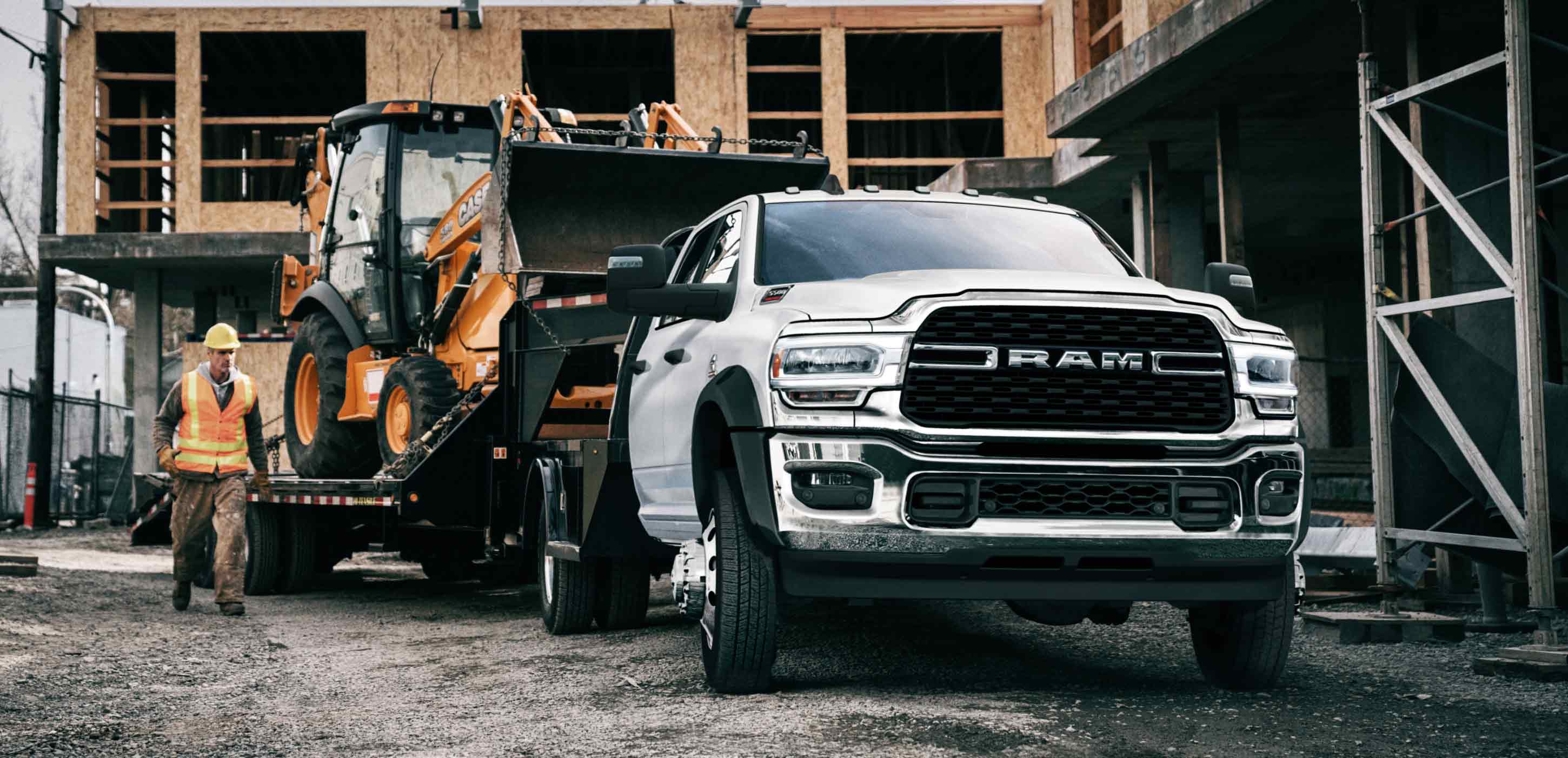 Display A white 2024 Ram 5500 SLT Chassis Cab Crew Cab on a construction site with an excavator in tow.