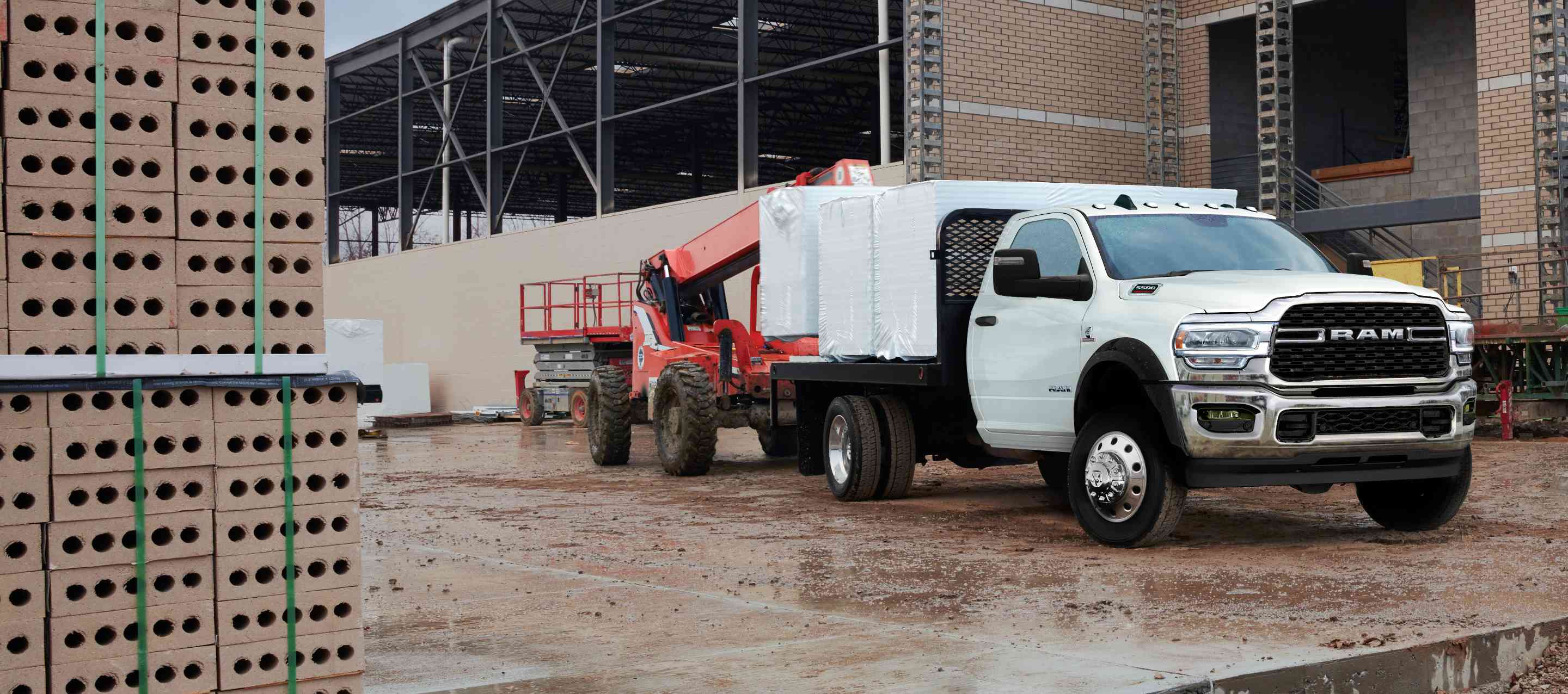 A blue 2023 Ram 5500 Limited Chassis Cab 4x4 Crew Cab with utility bed upfit, parked at a commercial building site.
