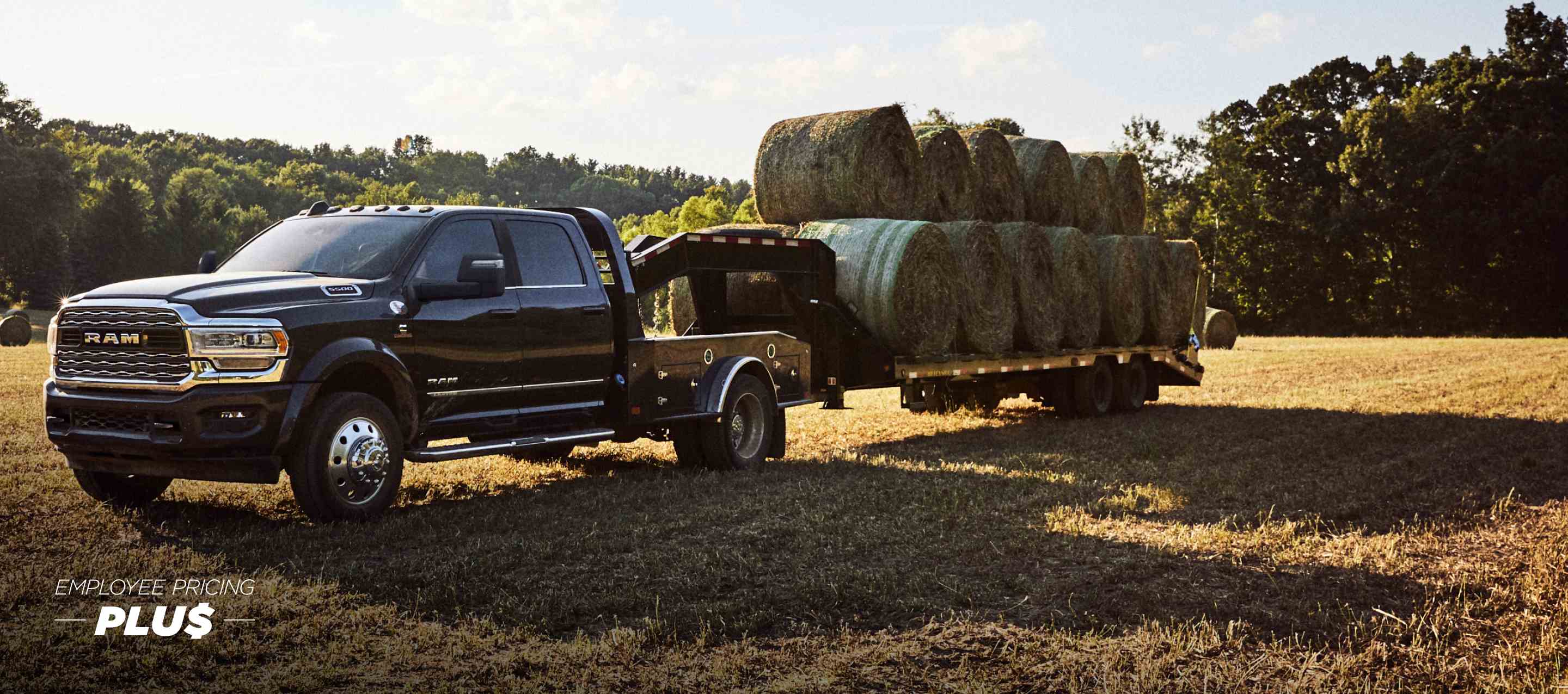A black 2024 Ram 5500 Limited 4x4 Chassis Crew Cab with a gooseneck trailer loaded with several bales of hay, parked in an open field. Employee Pricing Plus Sales Event.