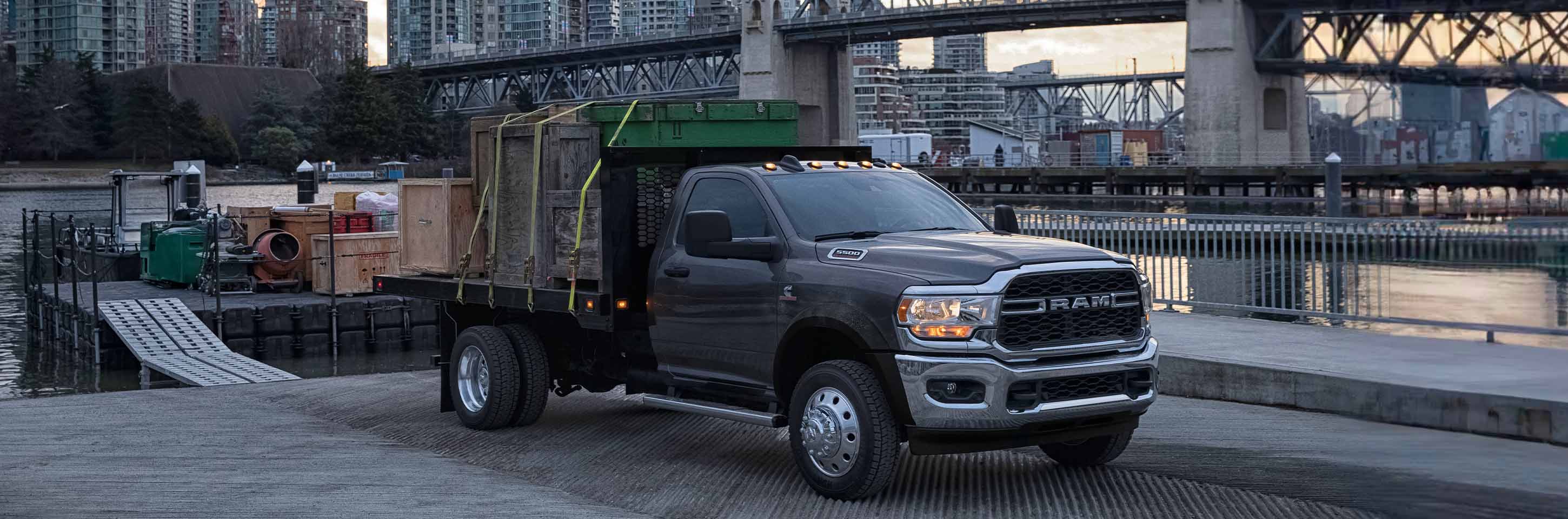 A gray 2024 Ram 5500 Tradesman Chassis Cab Regular Cab parked at a riverside dock and loaded with wooden crates.