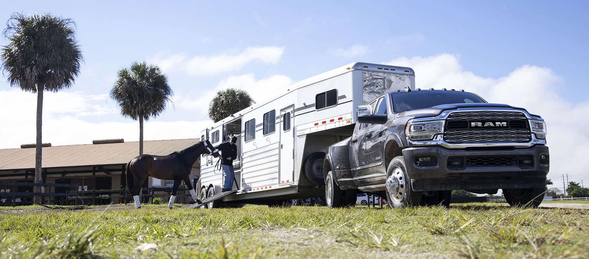 A 2024 Ram 3500 Limited Mega Cab towing a fifth wheel horse trailer with a man leading a horse into the trailer.