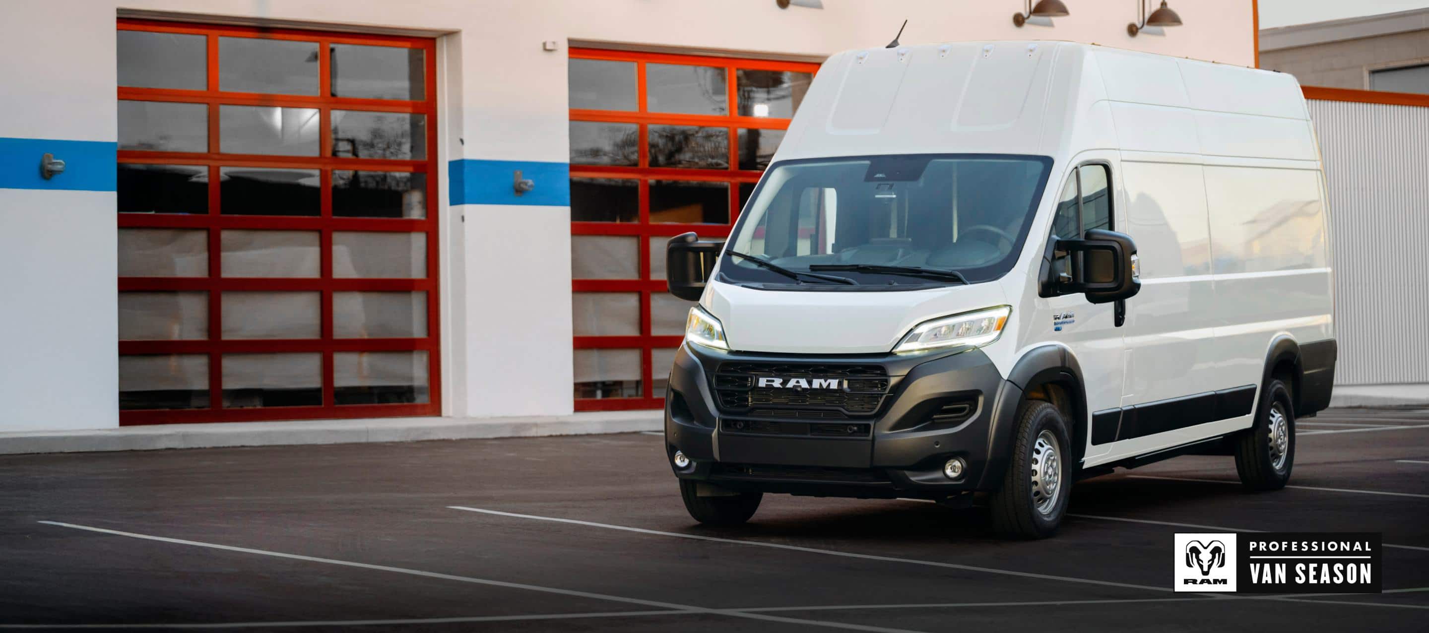A driver-side front angle of a white 2024 Ram ProMaster EV 3500 Super High Roof Step Van parked near a commercial garage. Ram Professional Van Season.