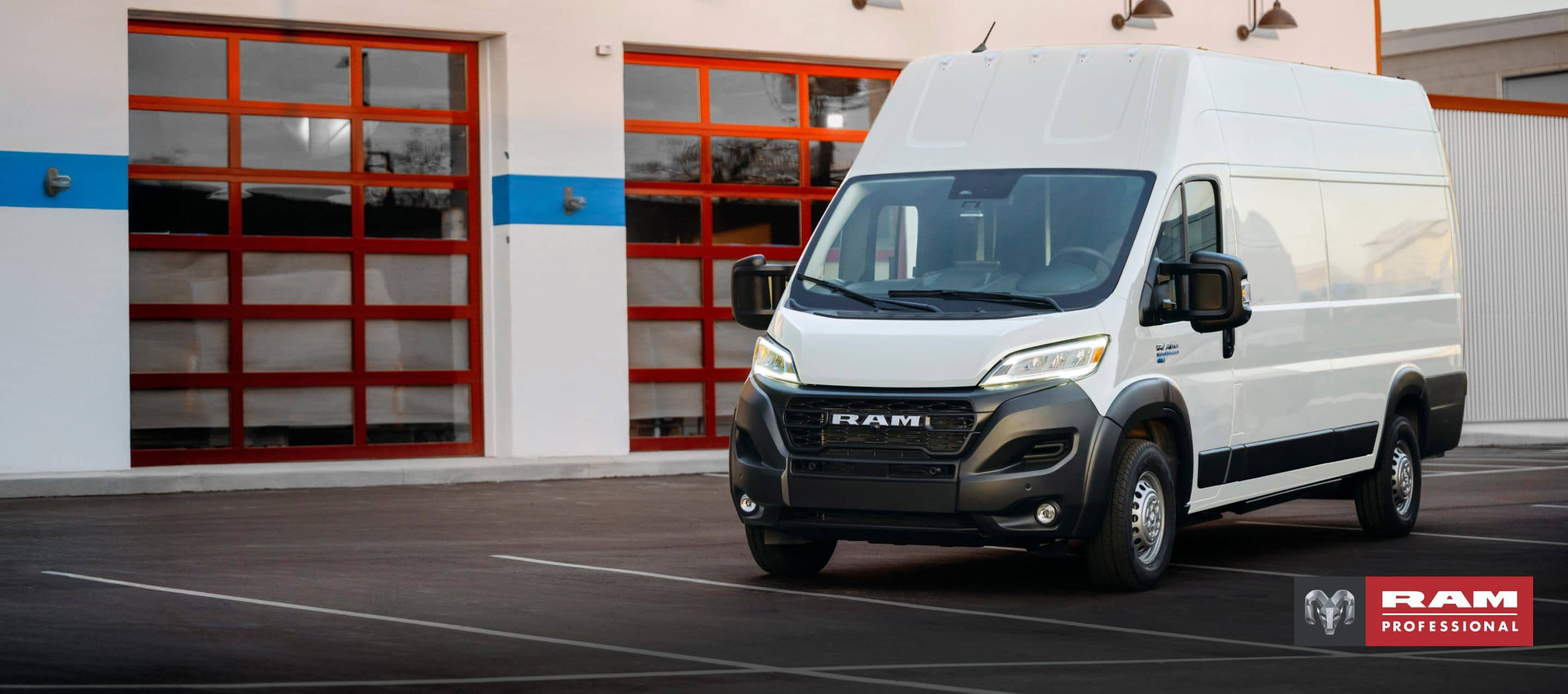 A driver-side front angle of a white 2024 Ram ProMaster EV 3500 Super High Roof Step Van parked near a commercial garage. Ram Professional.