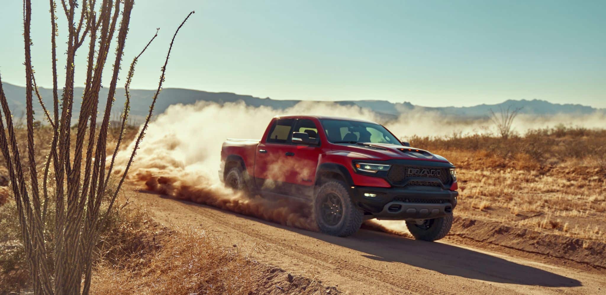 Display A red 2024 Ram 1500 TRX Crew Cab being driven off-road in the desert with dust rising from its wheels.