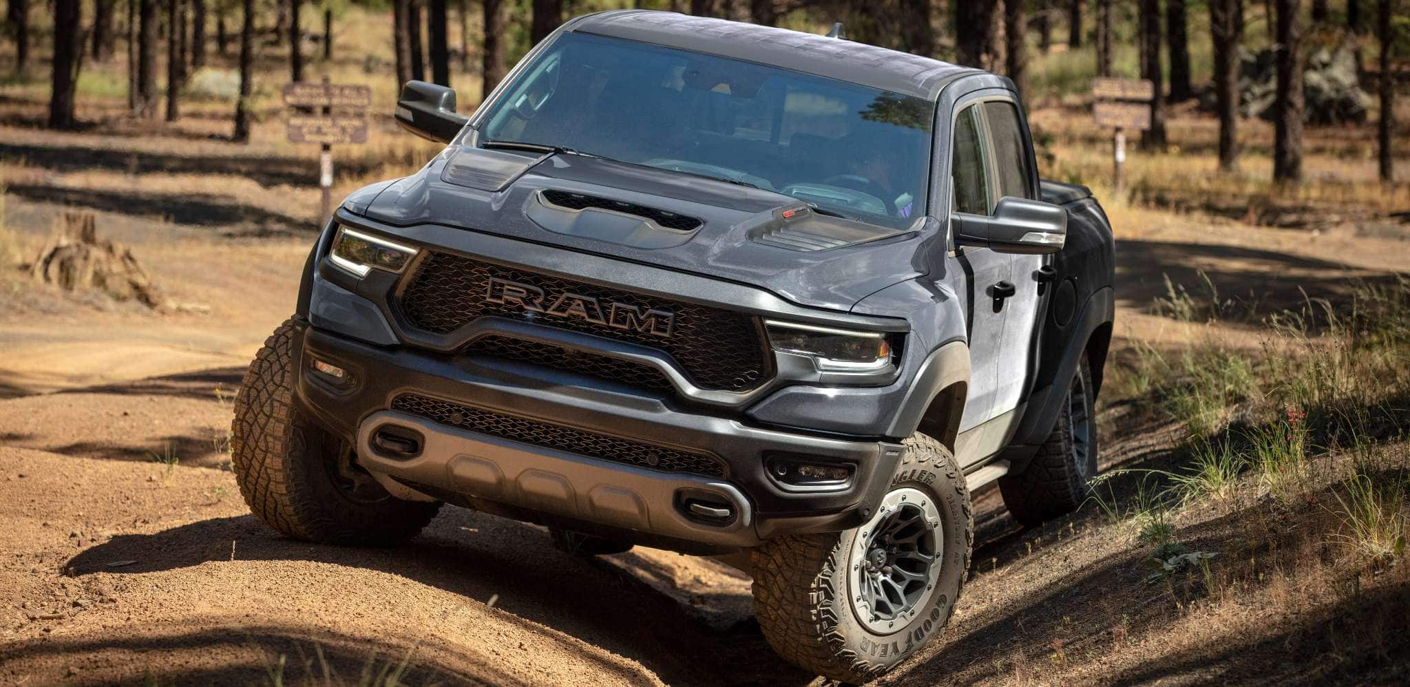 Display The 2024 Ram 1500 TRX Crew Cab being driven off-road on uneven terrain, with the front driver-side wheel in a shallow ditch and the other wheels elevated.