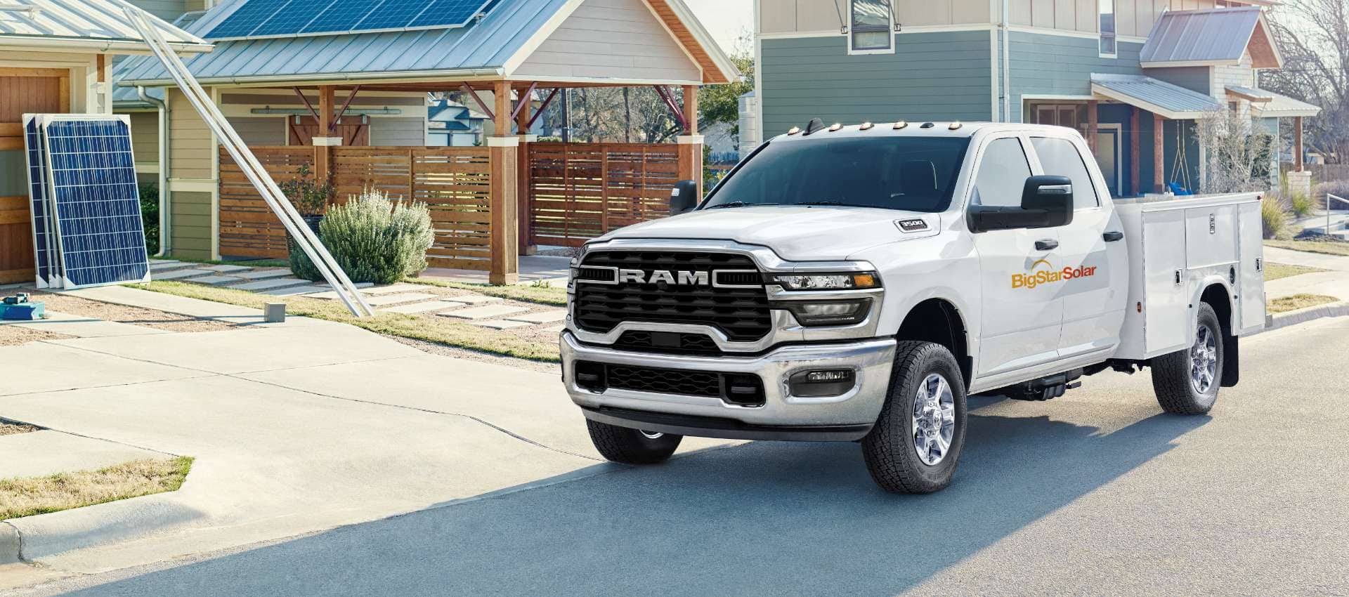 A white 2025 Ram 3500 Tradesman Chassis Cab Crew Cab with a service body upfit and a solar panel company logo on its driver's door, parked in a residential neighborhood under construction.