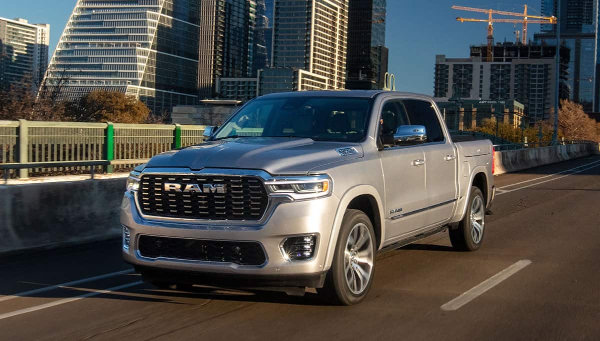 Display A silver 2025 Ram 1500 Tungsten Crew Cab being driven on a highway bridge in a city, with tall buildings in the background.