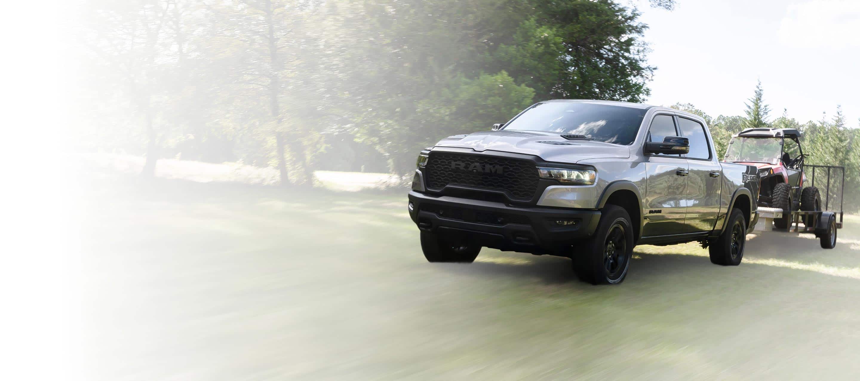 A gray 2025 Ram 1500 Rebel 4x4 Crew Cab towing an ATV on a utility trailer.