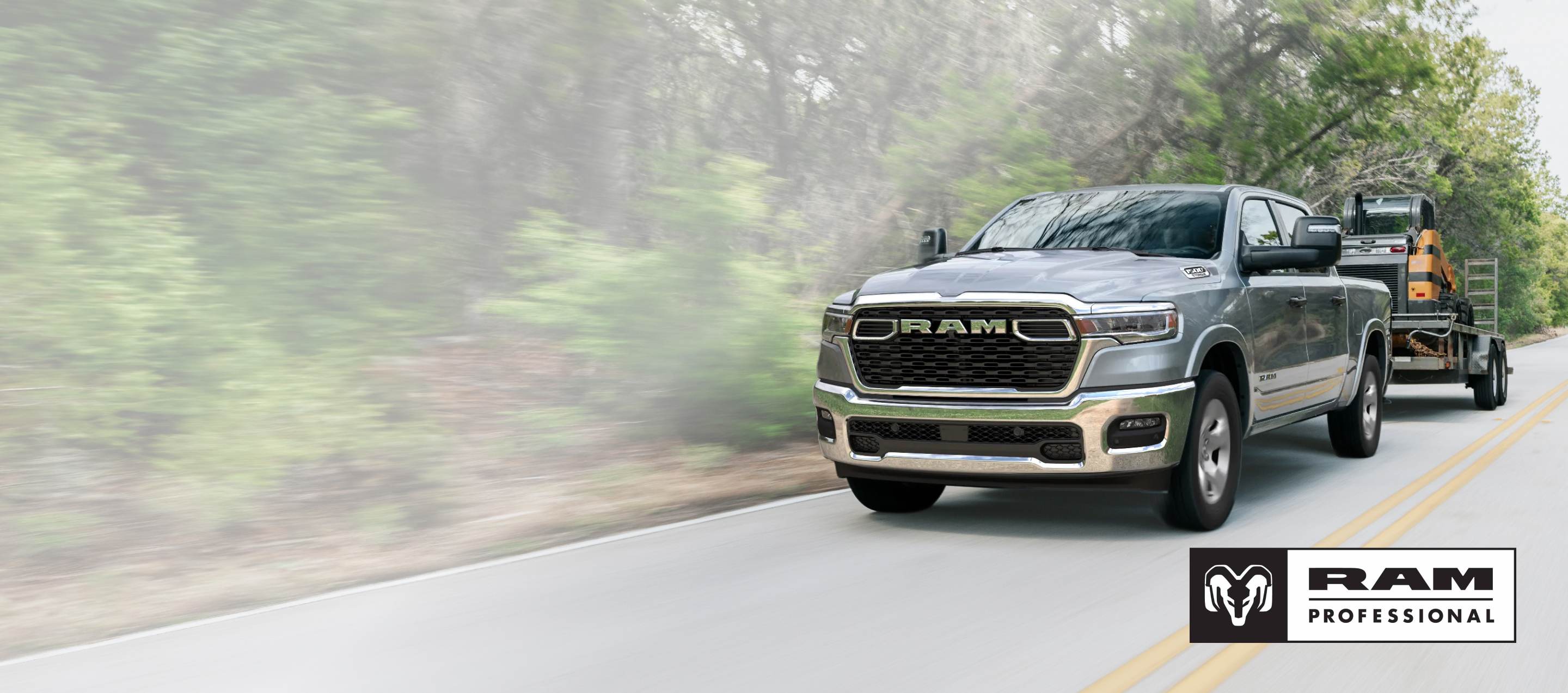 A silver 2025 Ram 1500 Big Horn 4x4 Crew Cab towing motorized equipment as it travels down a highway. Ram Professional.