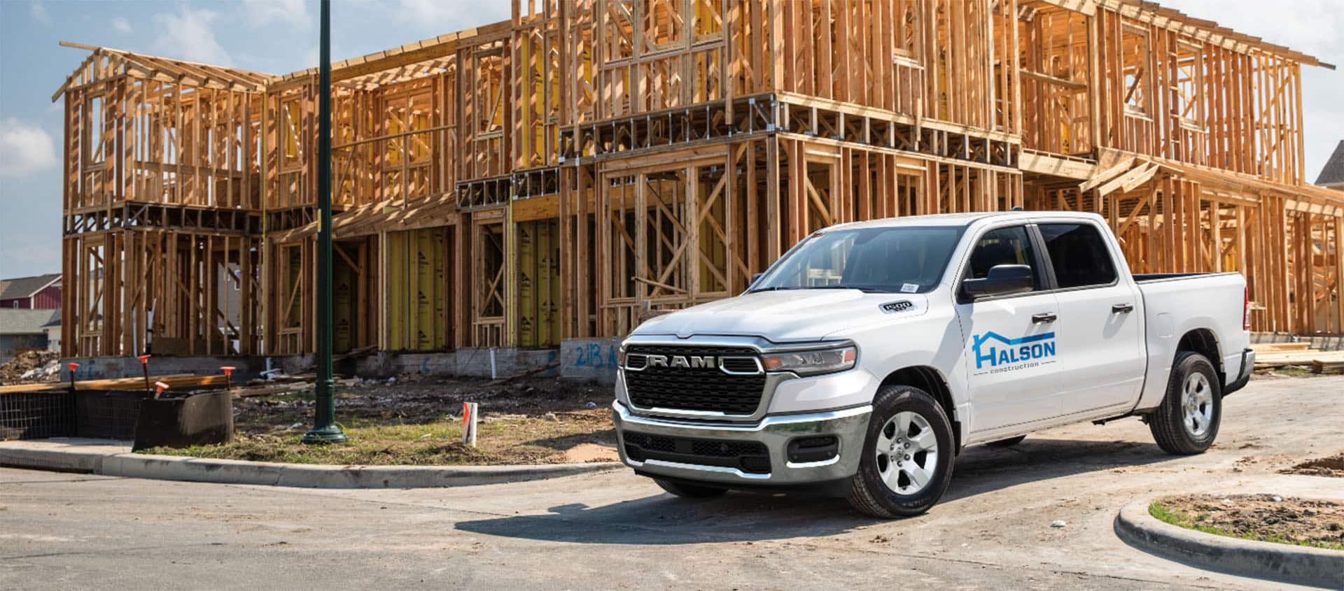 A white 2025 Ram 1500 Tradesman 4x4 Crew Cab with a construction company's signage on its driver's door, parked at a building site.