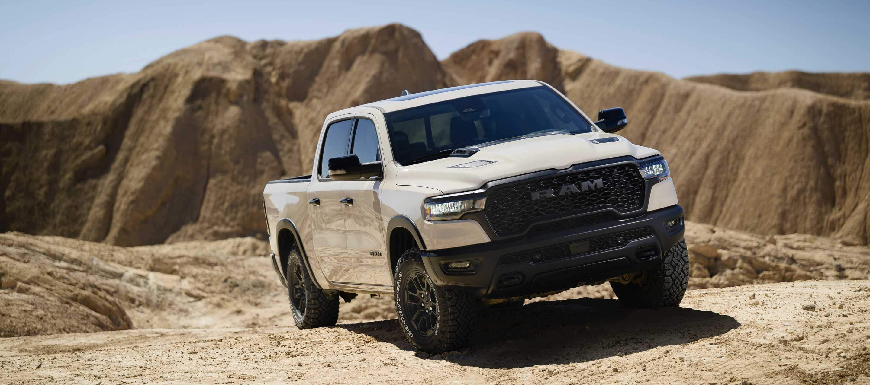 A front passenger-side angle of a white 2025 Ram 1500 Rebel X Crew Cab being driven on a hill off-road in the desert.