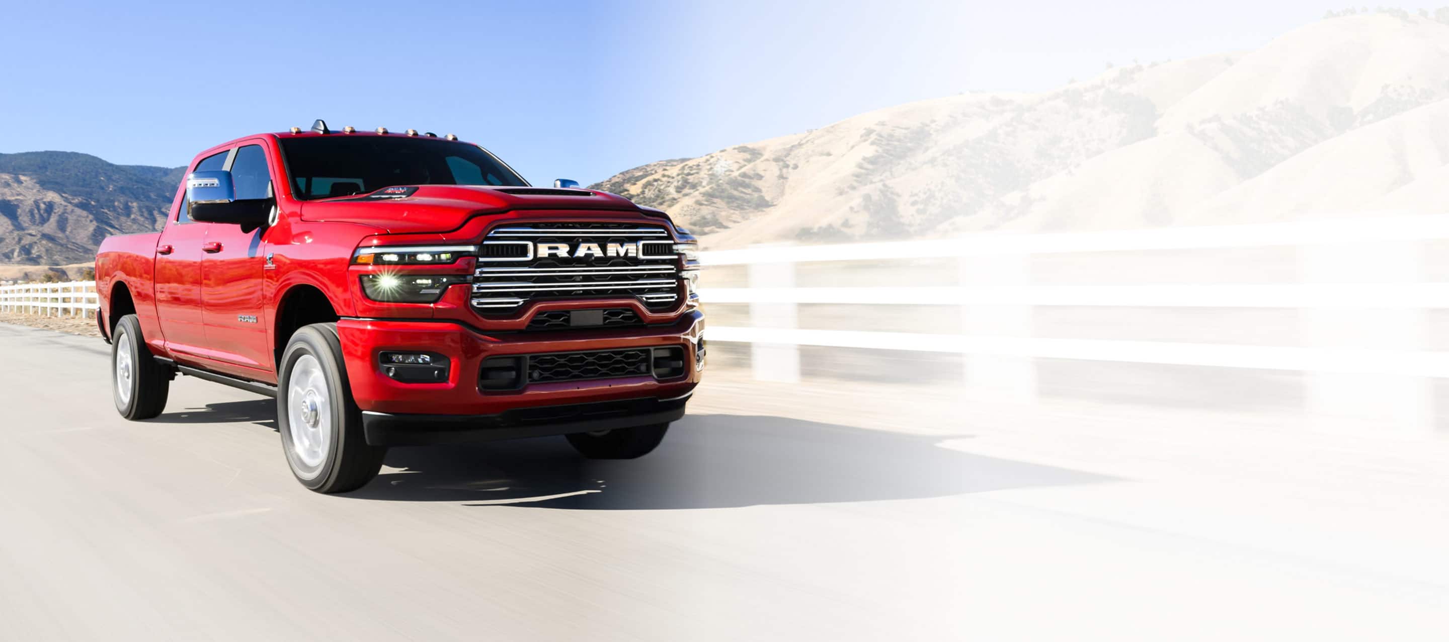 A red 2025 Ram 2500 Laramie 4x4 Crew Cab traveling on a highway beside a ranch in the desert.