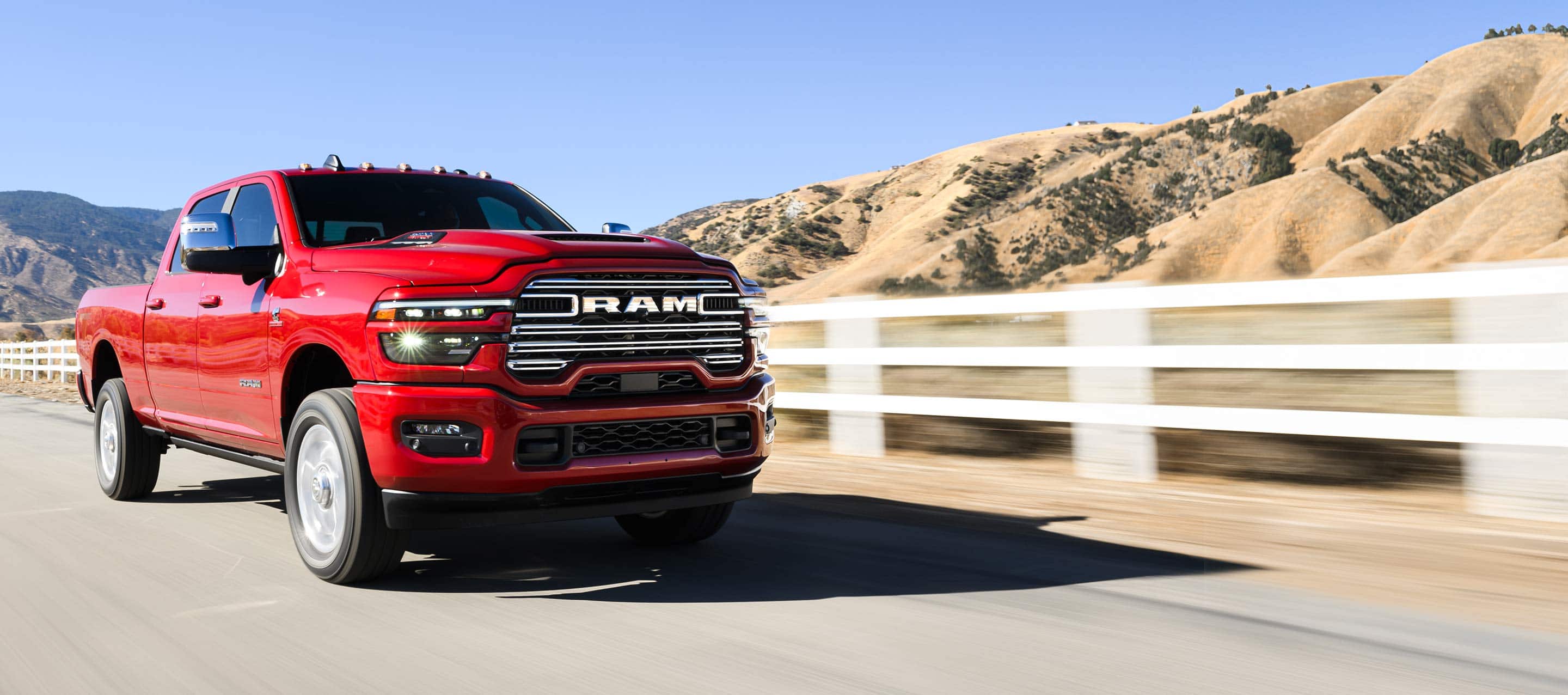 A red 2025 Ram 2500 Laramie 4x4 Crew Cab traveling on a highway with mountains in the background.