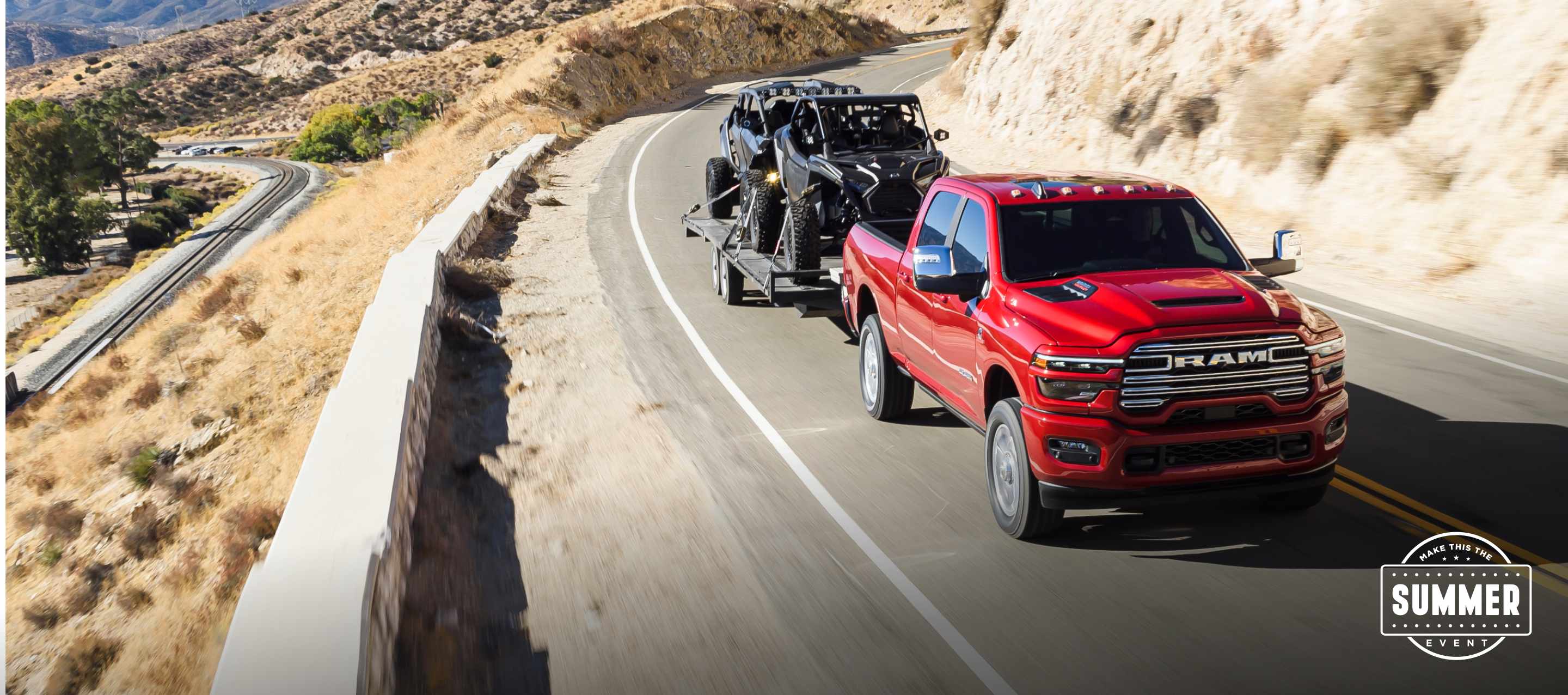 A red 2025 Ram 2500 Laramie 4x4 Crew Cab traveling on a highway in the mountains, while towing two ATVs.  Make This The Summer Event.