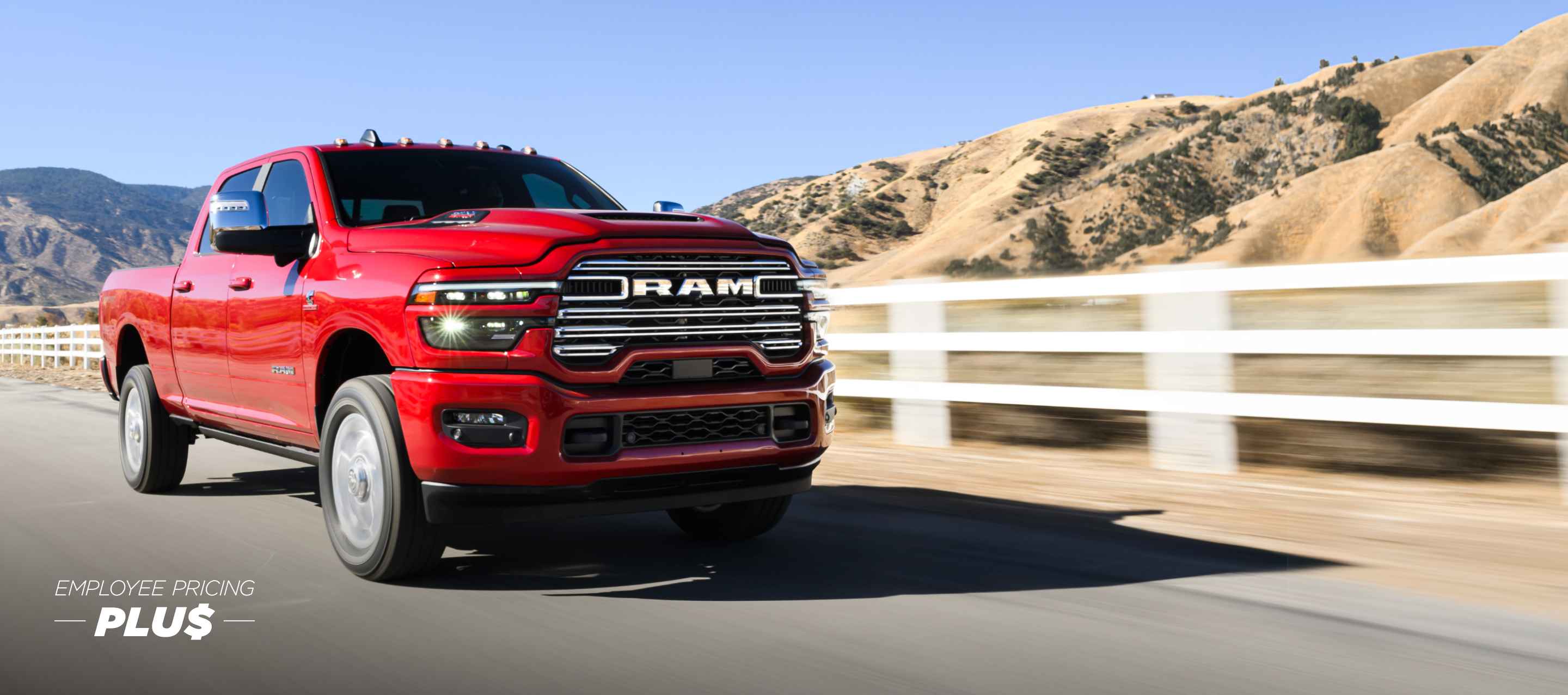 A red 2025 Ram 2500 Laramie 4x4 Crew Cab traveling on a highway with mountains in the background. Employee Pricing Plus Sales Event.