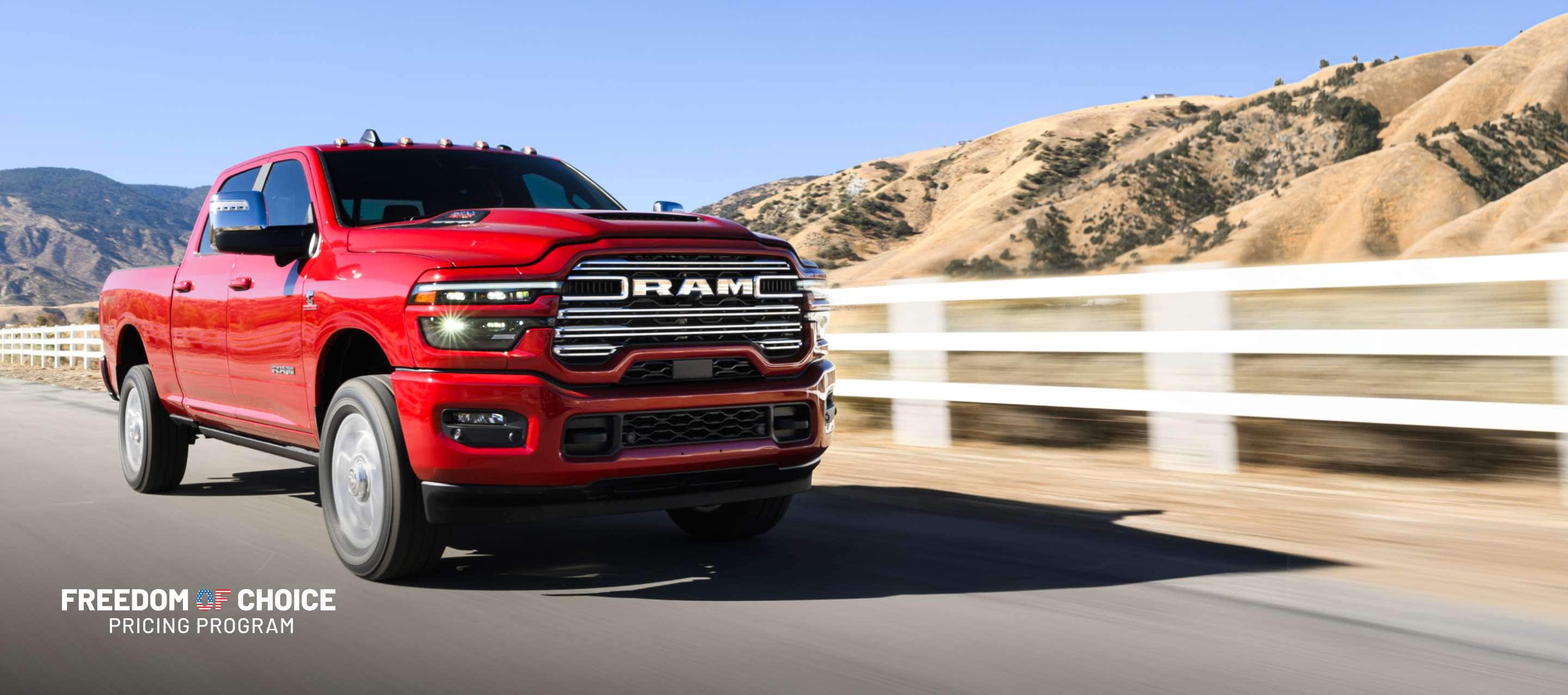 A red 2025 Ram 2500 Laramie 4x4 Crew Cab traveling on a highway with mountains in the background.  Freedom Of Choice Pricing Update Sales Event.