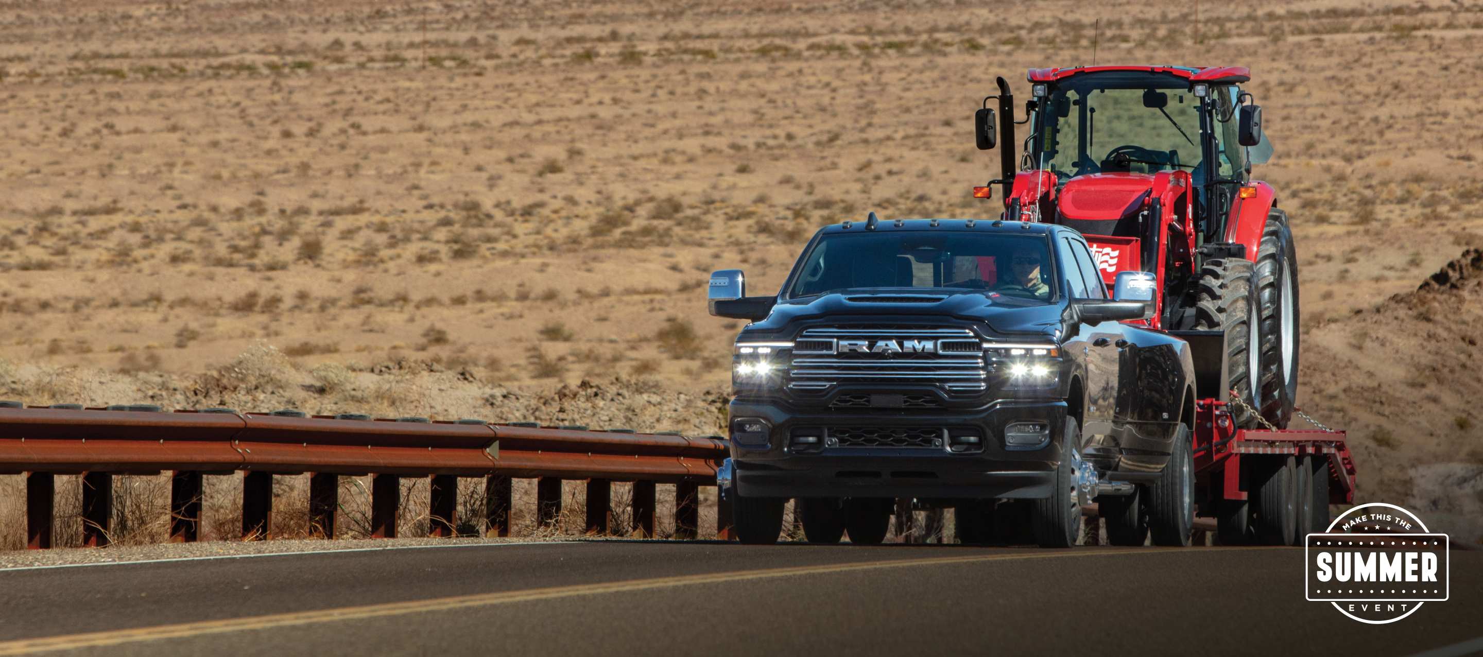 A 2025 Ram 3500 Limited 4x4 Crew Cab towing a construction vehicle on a fifth-wheel flatbed trailer as it travels on a highway in the desert. Make This The Summer Event.
