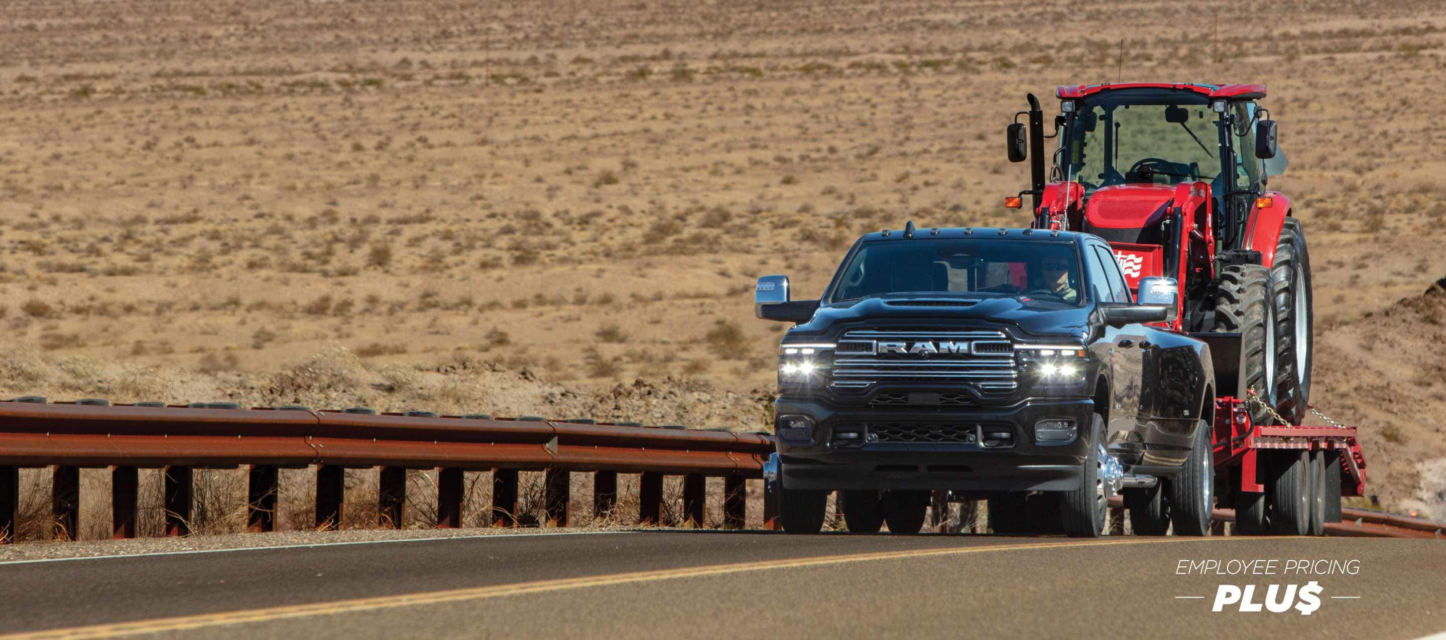 A 2025 Ram 3500 Limited 4x4 Crew Cab towing a construction vehicle on a fifth-wheel flatbed trailer as it travels on a highway in the desert. Employee Pricing Plus Sales Event.