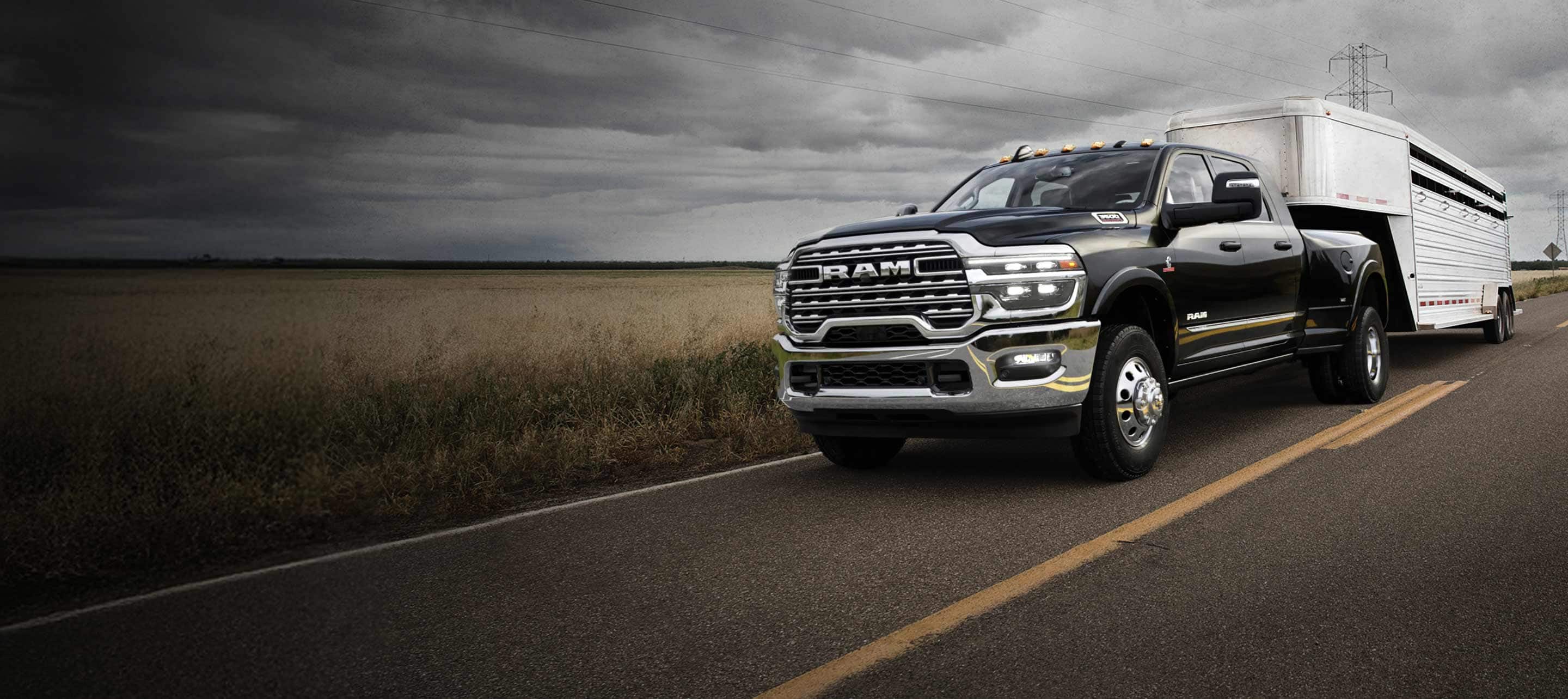 A black 2025 Ram 3500 Limited 4x4 Mega Cab traveling down a highway, towing a large travel trailer with storm clouds overhead.