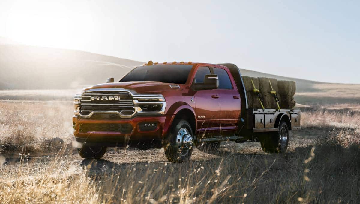 Display A red 2025 Ram 5500 Laramie Chassis Crew Cab carrying several large bales of hay on a long platform upfit.